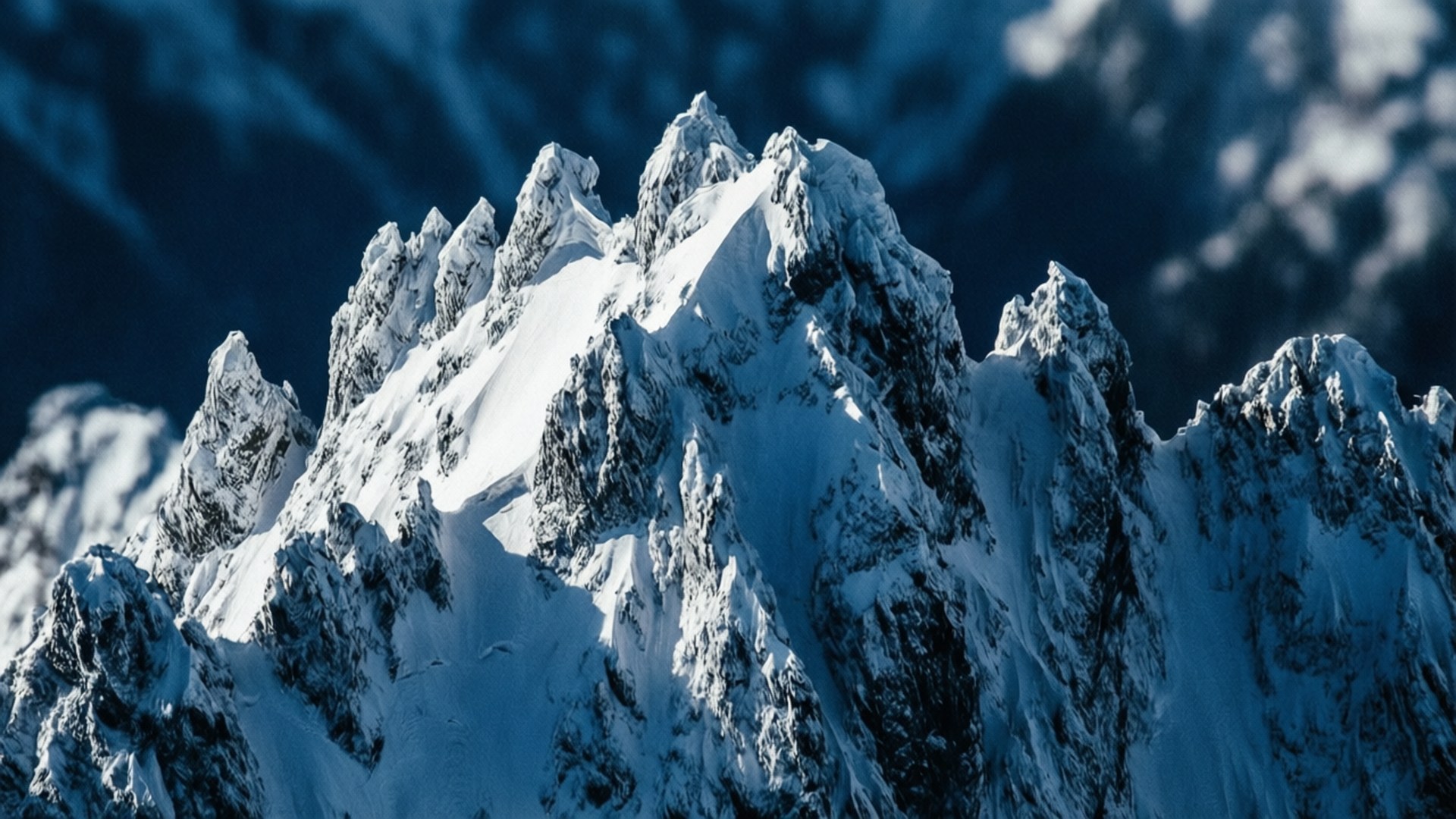 Jagged Ridge Abstract 壁紙 — 一座鋸齒狀的雪山山峰在深藍色的天空和縷縷白雲中 sharply 聳立。