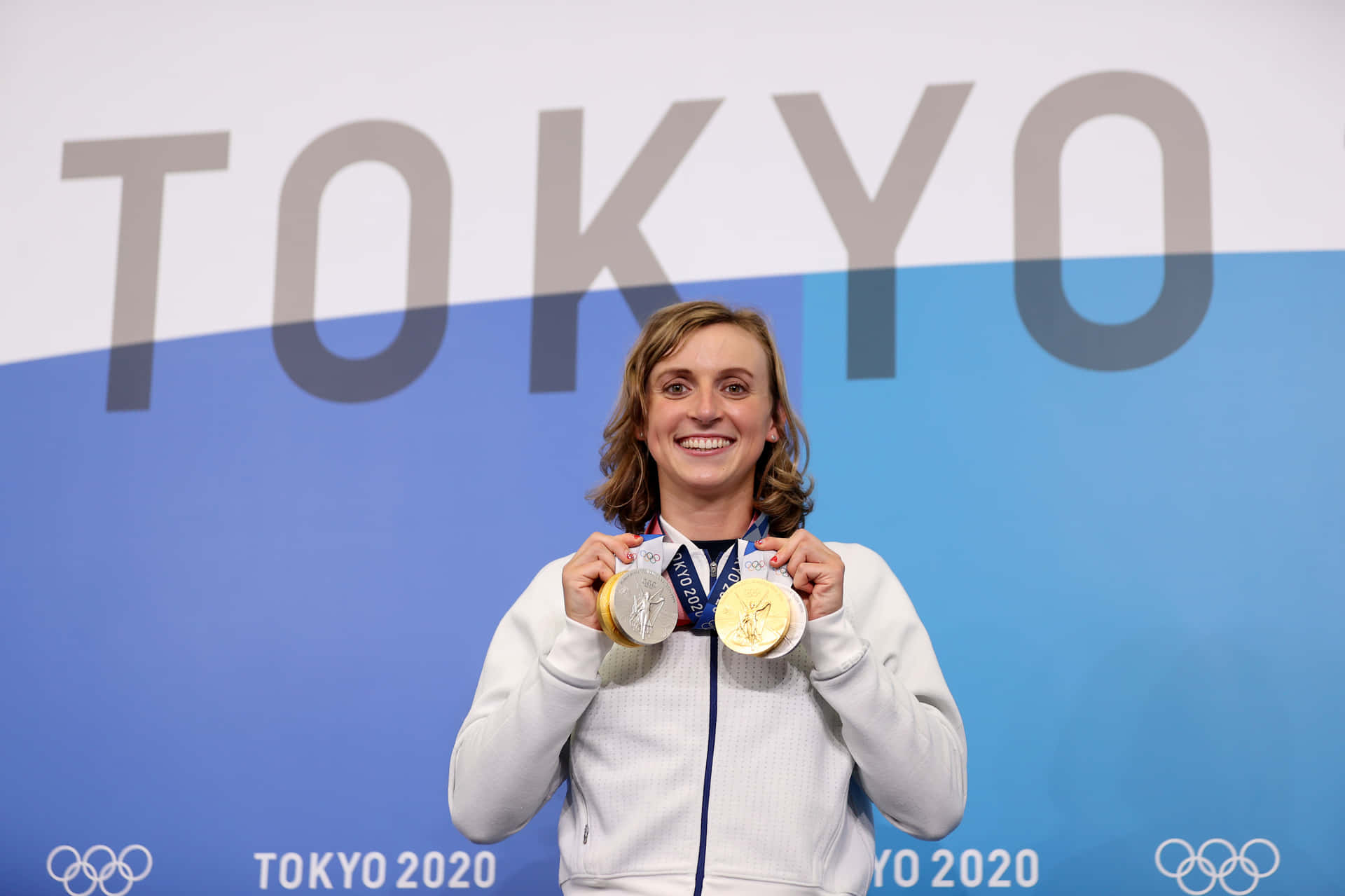  壁紙 — 一位快樂的女泳將在東京2020背景下自豪地展示她的三枚奧運獎牌，笑容燦爛。