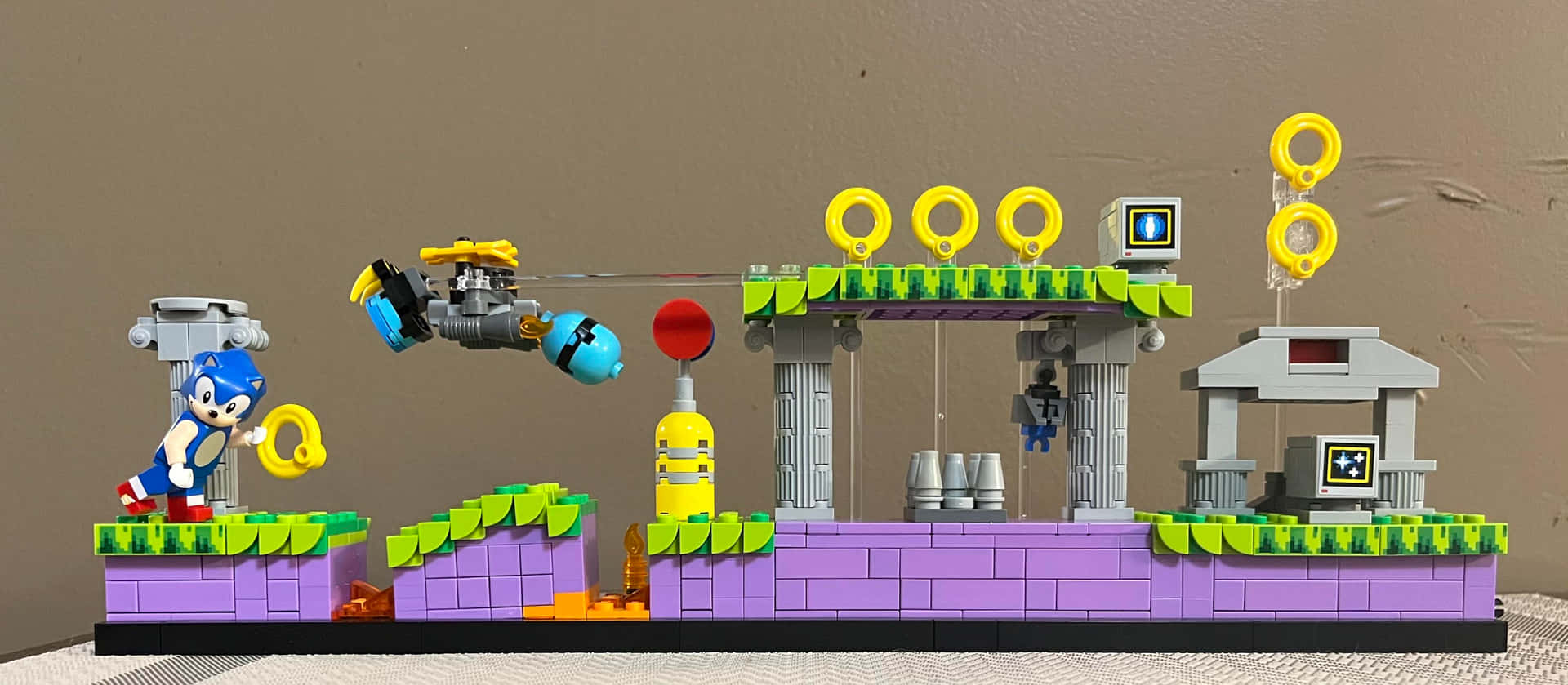  壁紙 — 一個LEGO Sonic the Hedgehog場景，包含圓環、平台和飛行車輛，背景為素色牆壁。
