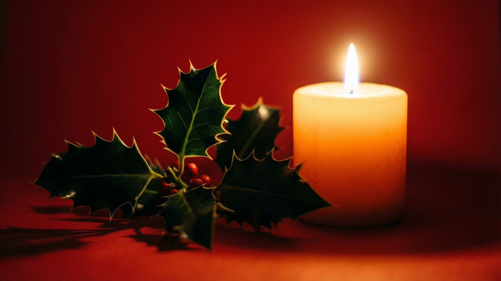 Candle and Holly on Red 壁紙 — 一支點燃的白色蠟燭在深紅色背景前，旁邊放著一枝帶有紅色漿果的冬青枝，散發著溫暖的光芒。