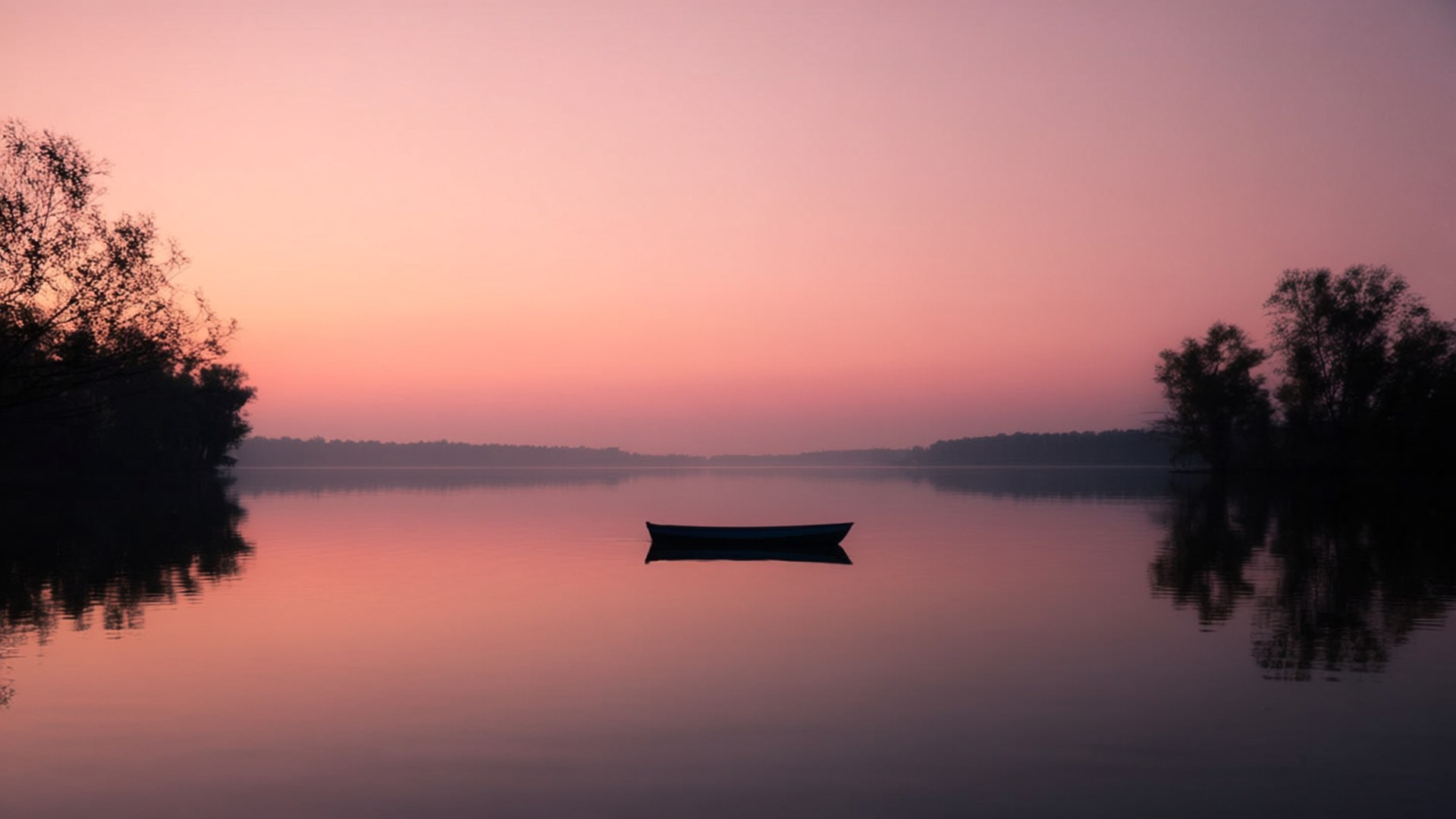 Inya Lake Sunset 壁紙 — 黎明時分，一艘孤獨的小船在霧氣瀰漫的湖上靜靜漂浮，粉紅和橙色的天空倒映在平靜的水面上，兩旁是黑暗的樹木剪影。