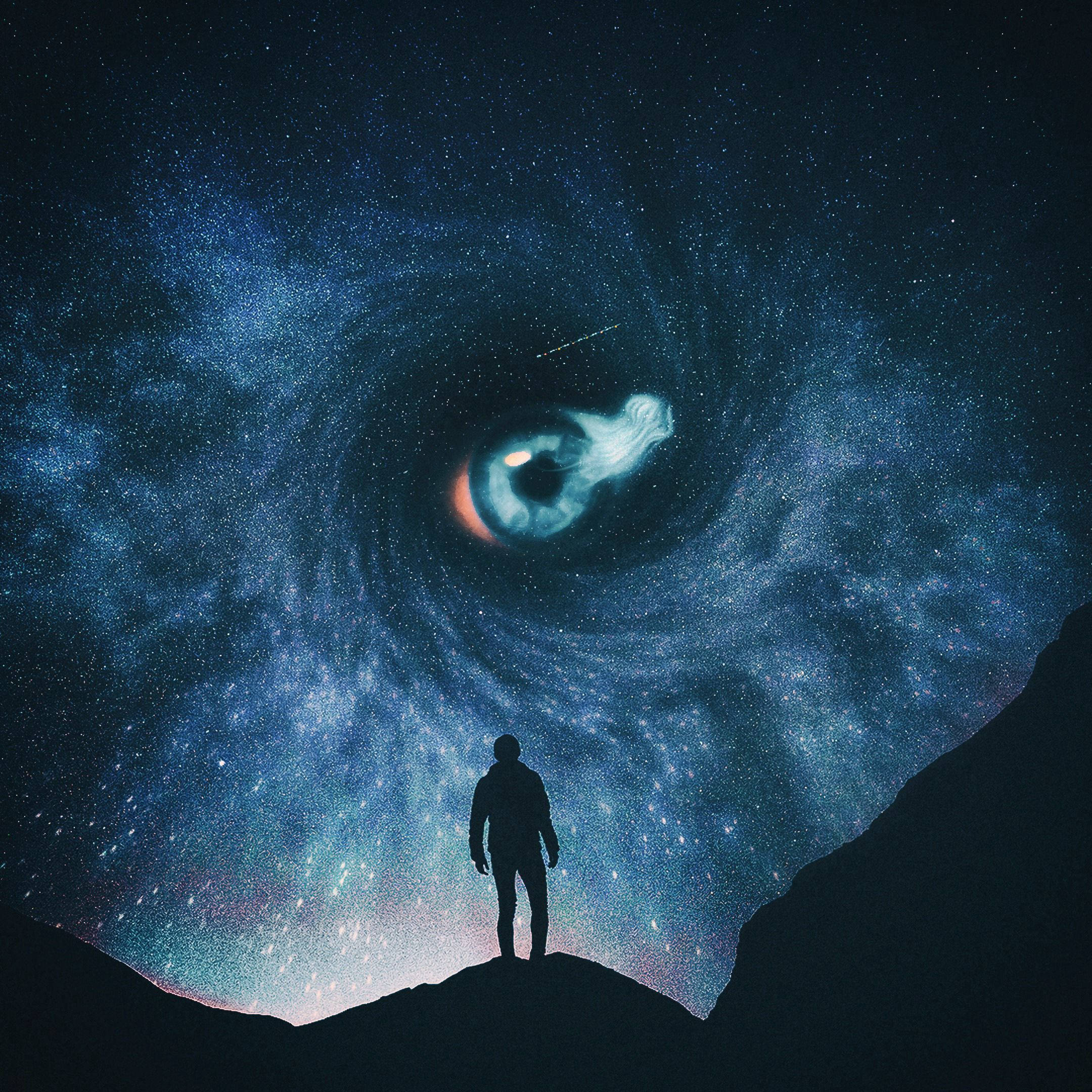 懸崖上一個人的剪影，凝視著夜空中巨大的宇宙之眼。 — iPad 壁紙