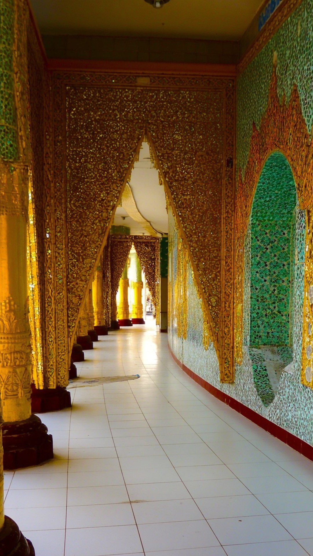 Botataung Pagoda Corridor 壁紙 — 一條長長的彎曲走廊，有金色華麗的柱子和綠色馬賽克牆壁，通向明亮的遠方門口。