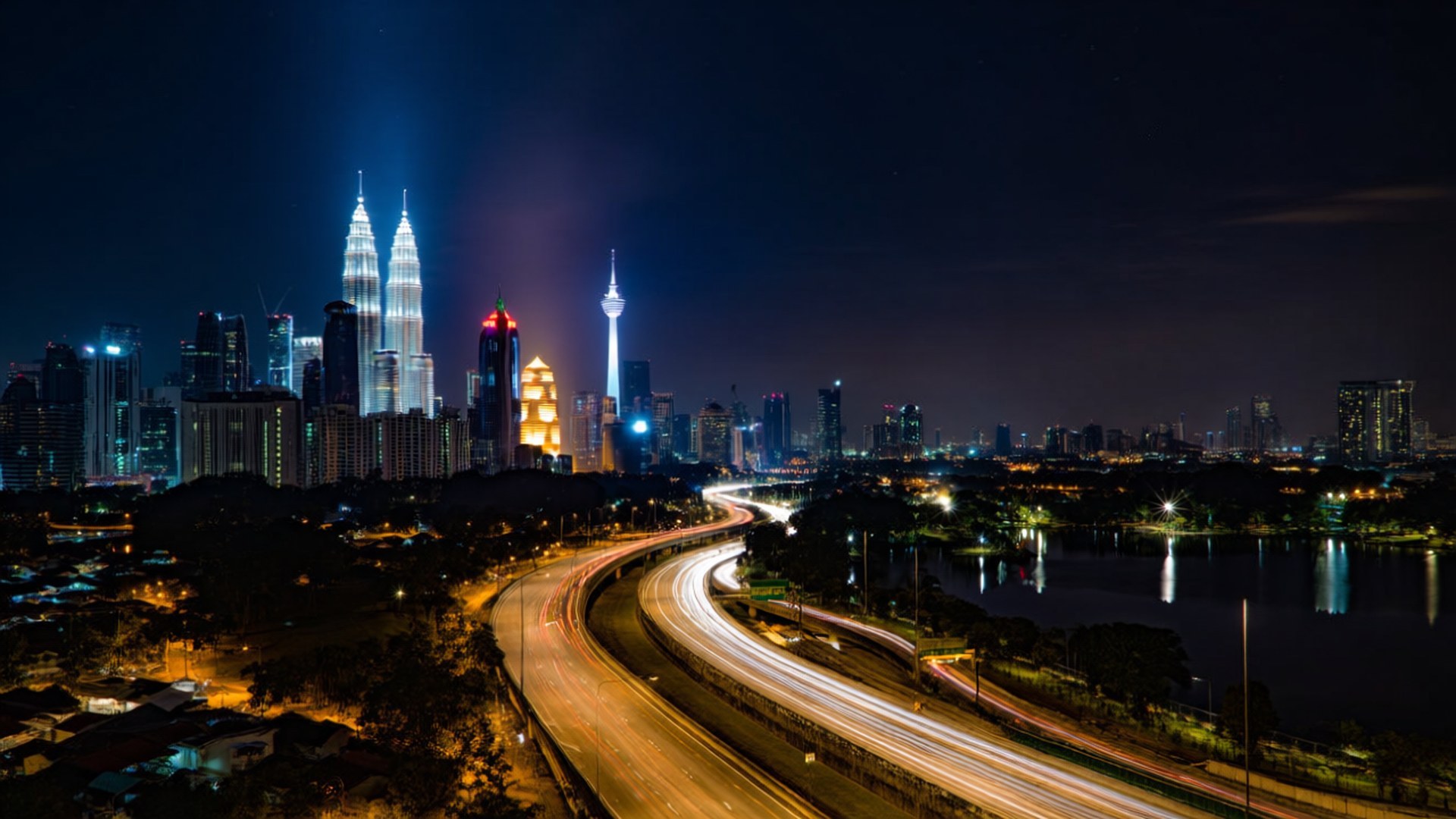 KL Night Lights 壁紙 — 長時間曝光的夜景照片捕捉到黑暗天空下閃爍的城市燈光和流動的交通，雙子星塔和吉隆坡塔被照亮。
