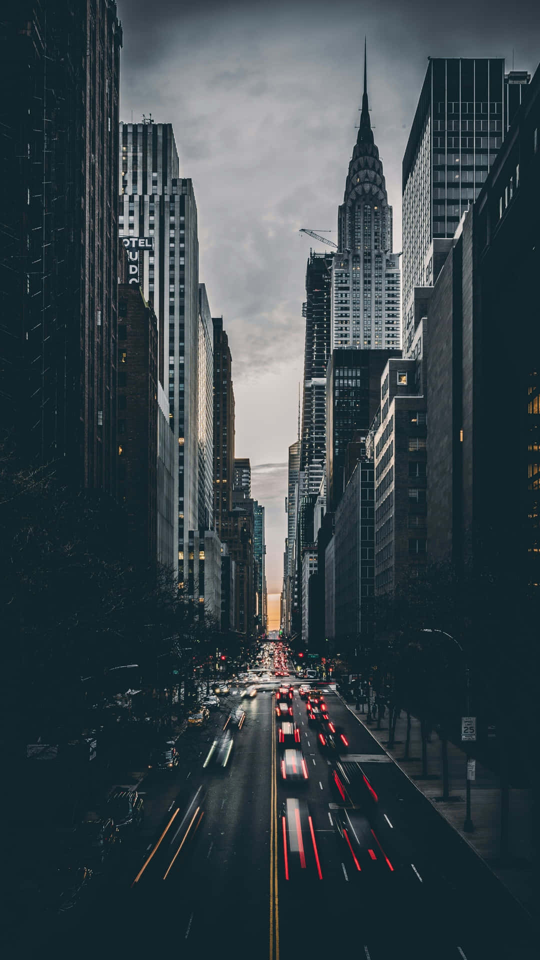  壁紙 — 一張在黃昏時分拍攝的繁華城市街道長曝光照片，車燈光線在高聳的摩天大樓之間流動。