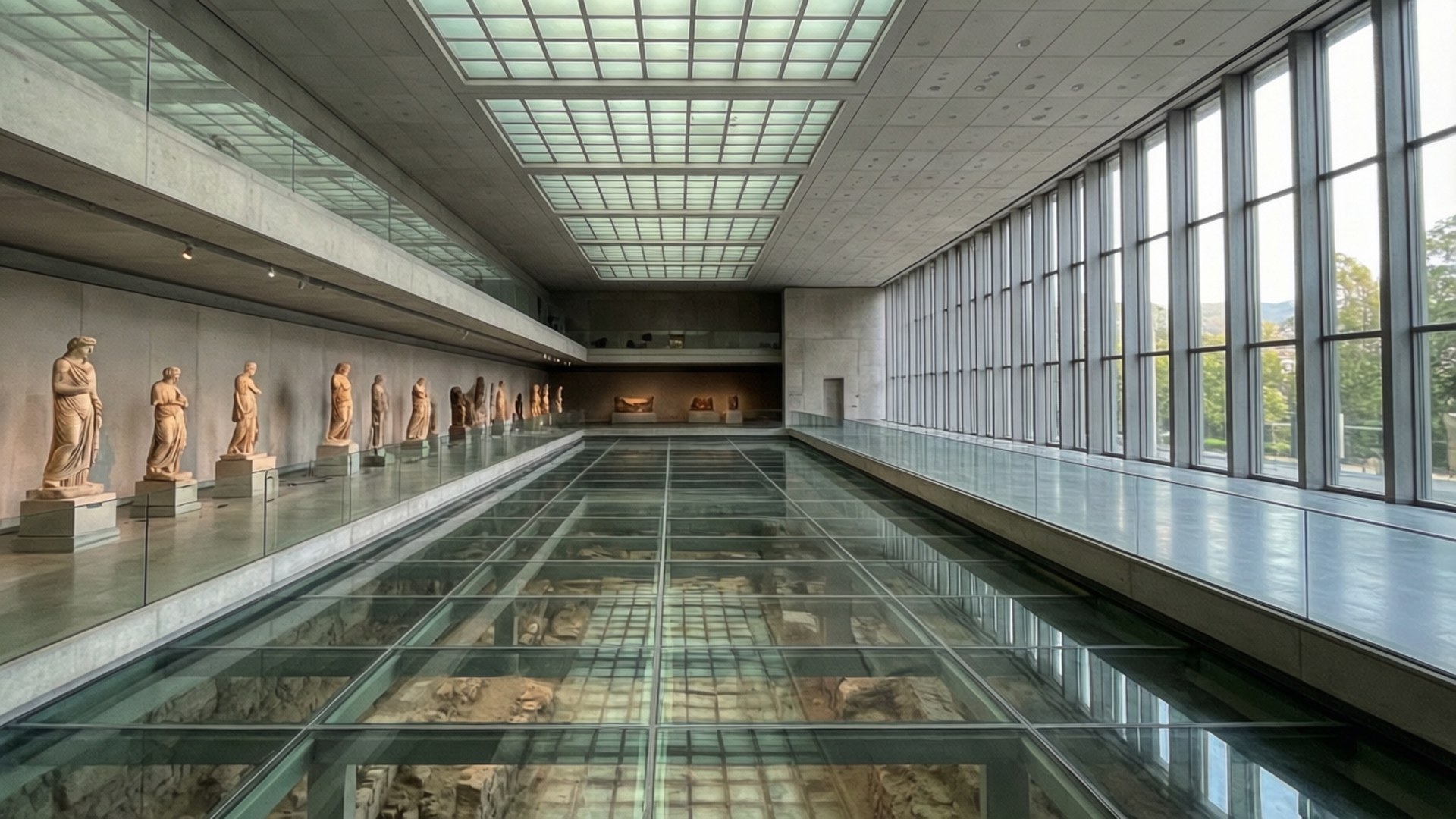 Acropolis Museum Interior 壁紙 — 長長的博物館畫廊，玻璃地板揭示下方的古代遺跡，天窗下的牆壁兩旁排列著古典雕像。