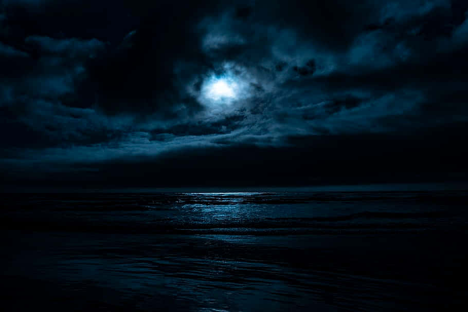  壁紙 — 一輪明亮的月亮穿透黑暗的暴風雲，在夜空下的洶湧海洋上投射出空靈的光芒。