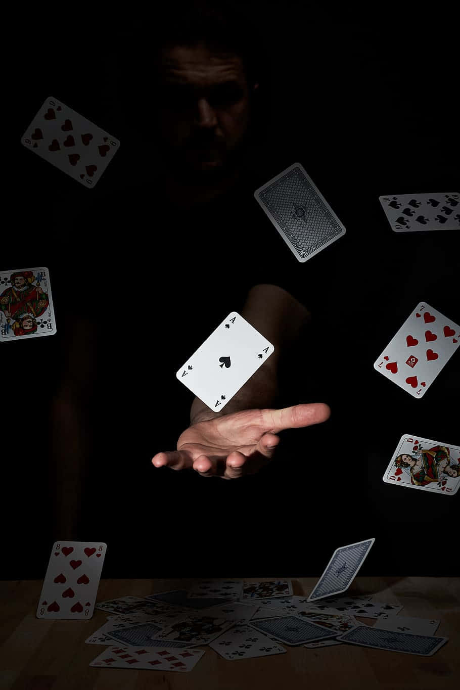  壁紙 — 魔術師的手在黑暗背景下懸浮於墜落的撲克牌上方，木桌上散落著紙牌。