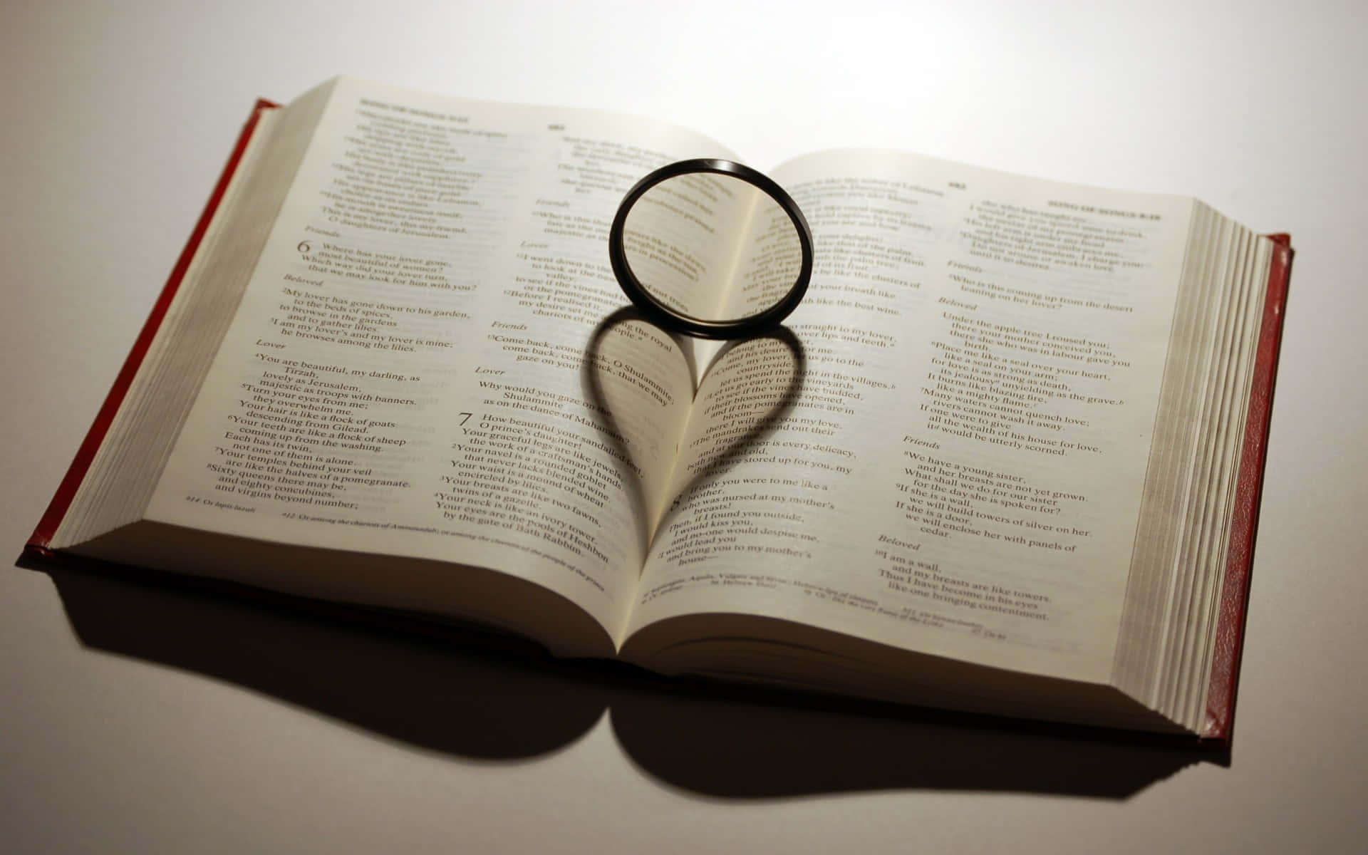 I Love God 桌布 壁紙 — 一個放大鏡放在一本打開的書上，顯露出密集的文字，柔和自然光線照亮書頁。