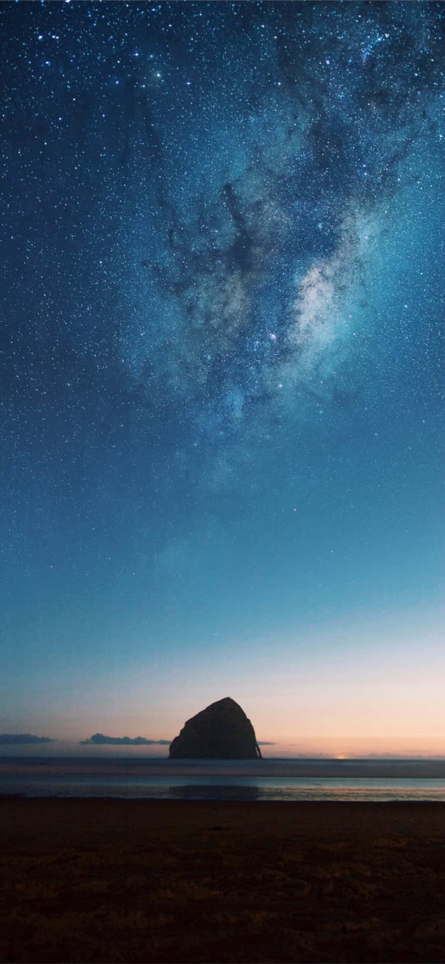  壁紙 — 一座雄偉的海蝕柱在佈滿銀河和星星的暮色天空下呈現剪影。