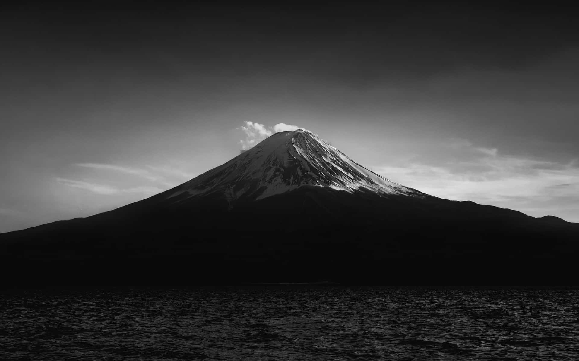 多雲天空下，黑暗湖泊上方的雪山輪廓。 — 日本黑白 壁紙
