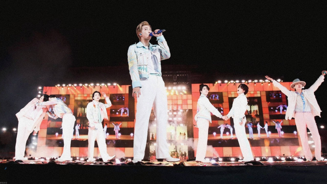 K-pop團體在夜晚燈光舞台上表演同步舞蹈動作。 — K Pop 壁紙