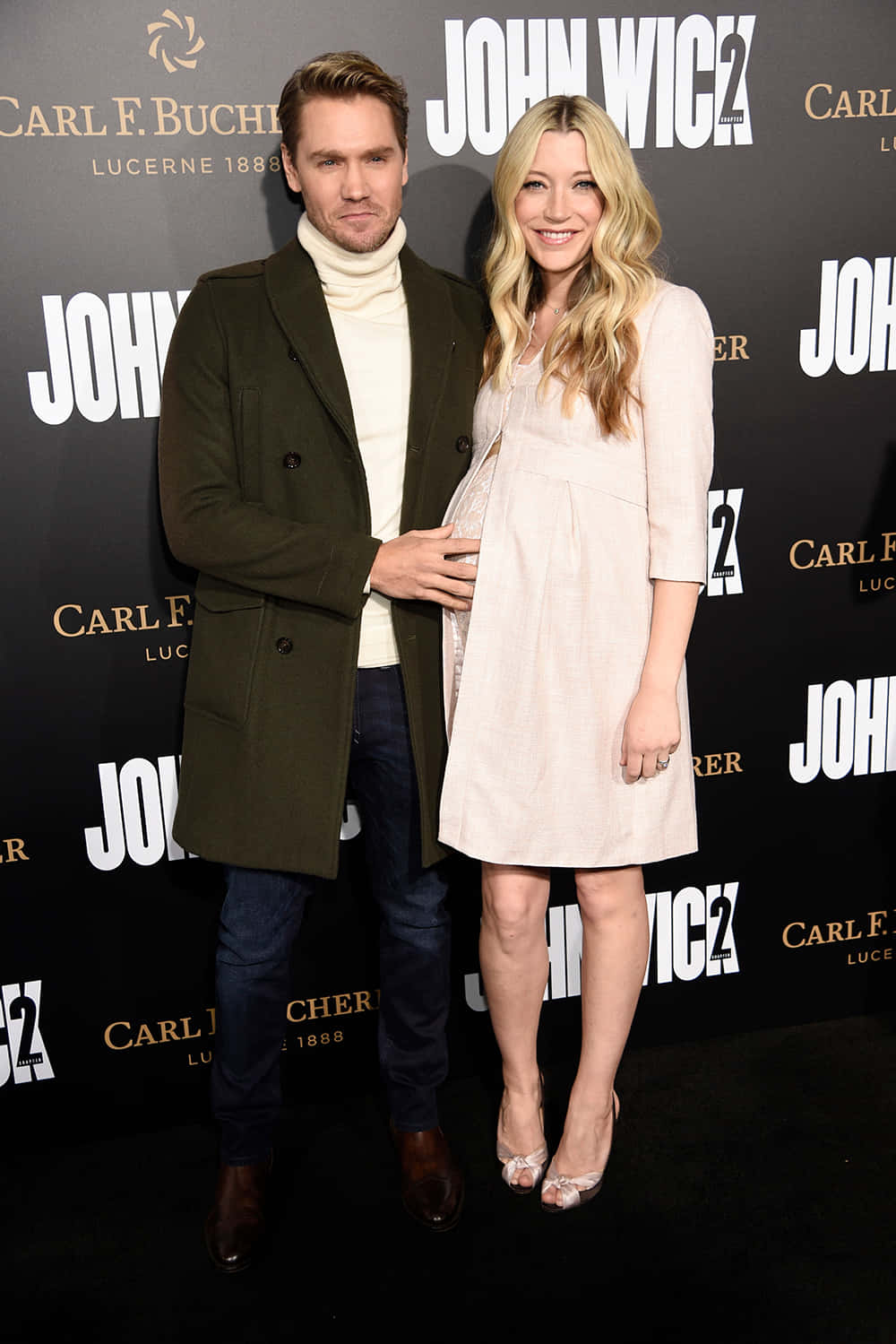 Sarah Roemer 桌布 壁紙 — 一名男子和一名孕婦在約翰維克2首映活動中一起擺姿勢，背景帶有品牌標誌。