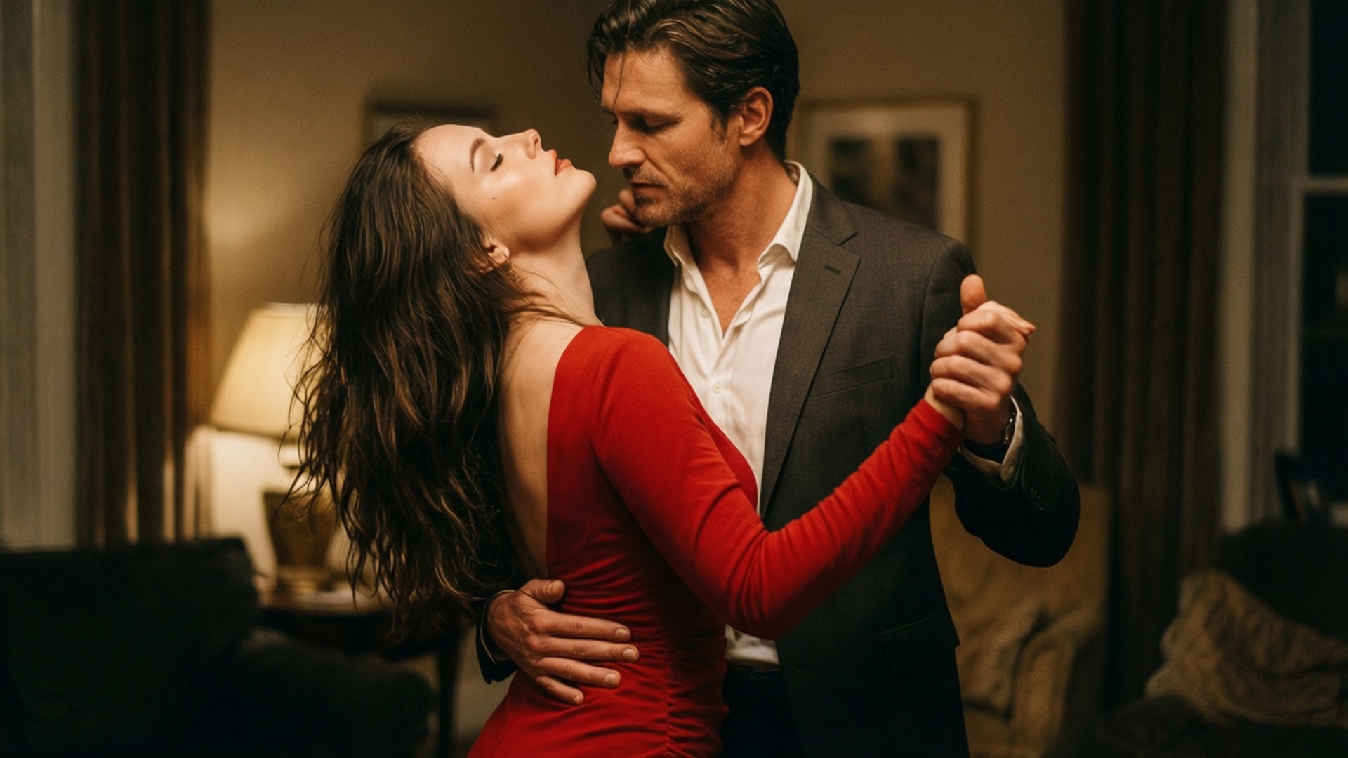Slow Dance Seduction 壁紙 — 一名身穿深色西裝的男子和一名身穿紅色連衣裙的女子在溫暖照明的客廳中親密跳舞。