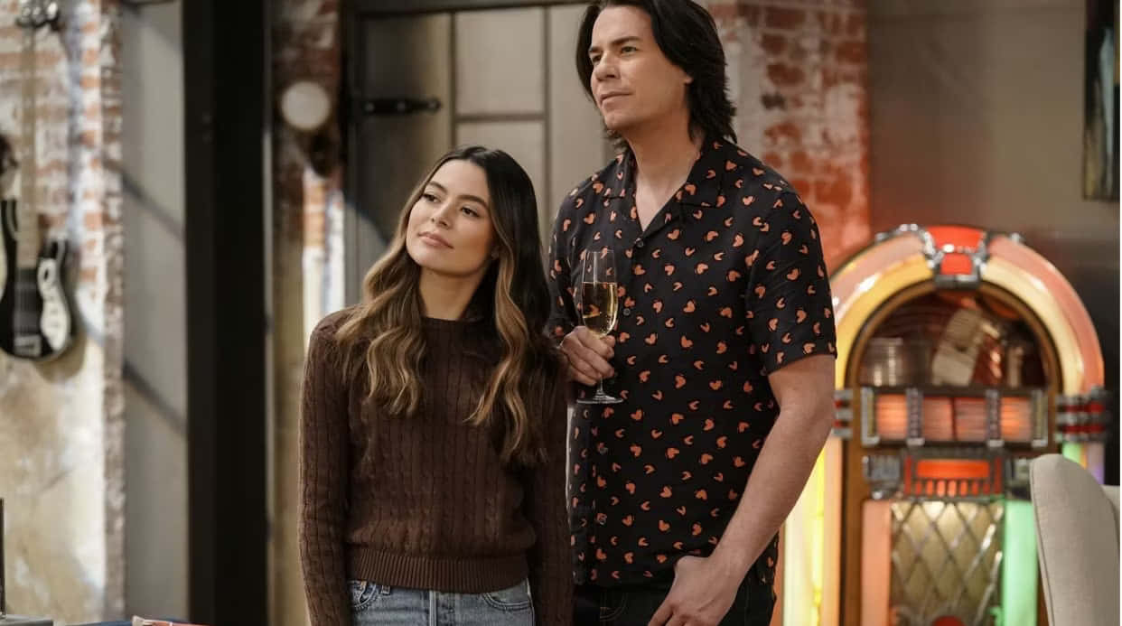  壁紙 — 一男一女站在一個以復古為主題的房間裡，房間有磚牆和一部復古點唱機，兩人都拿著飲料向上看。
