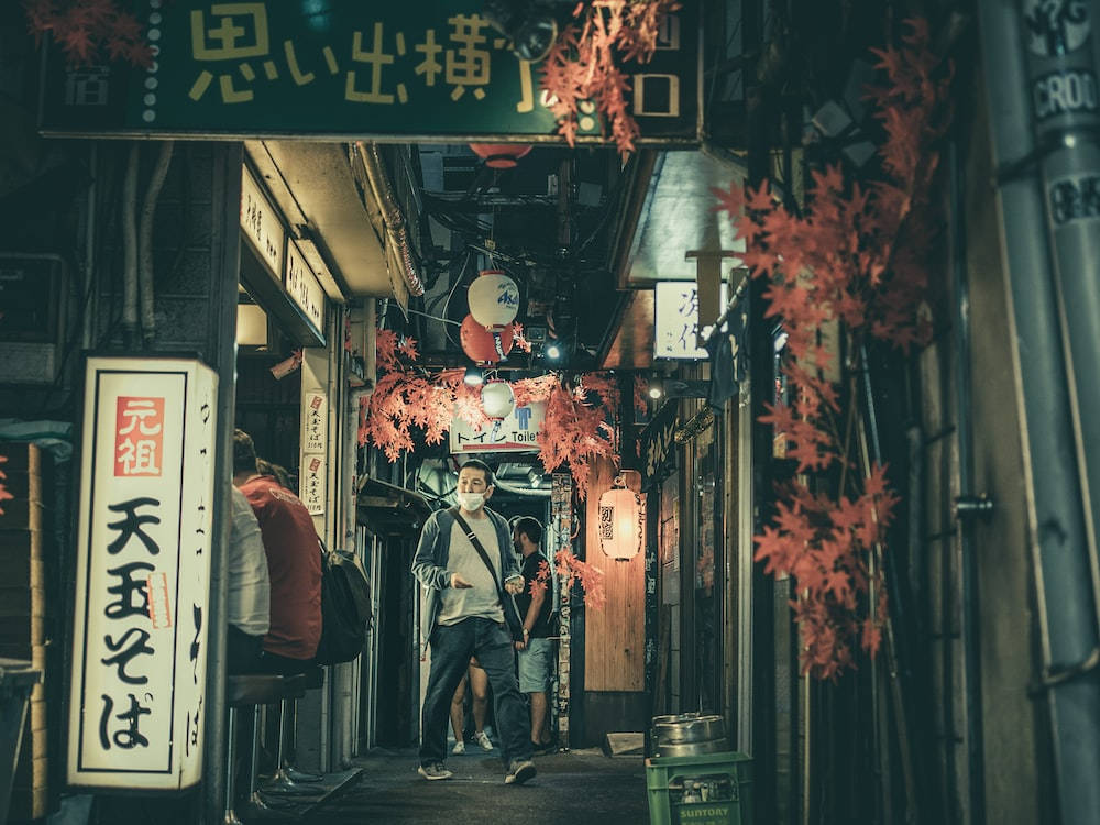夜晚，一個人走在狹窄的日本小巷中，有紅色楓葉裝飾和發光的招牌。
