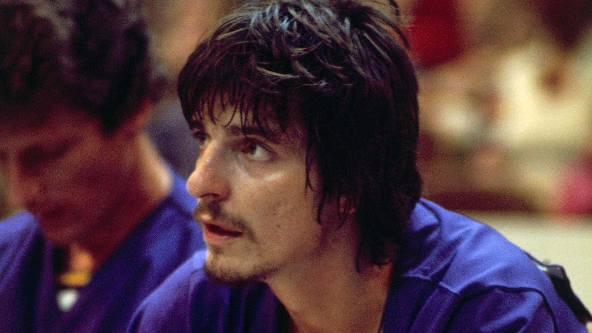 一個濕髮留鬚的男人穿著藍色襯衫，在室內專注地向前看。 — NBA 壁紙