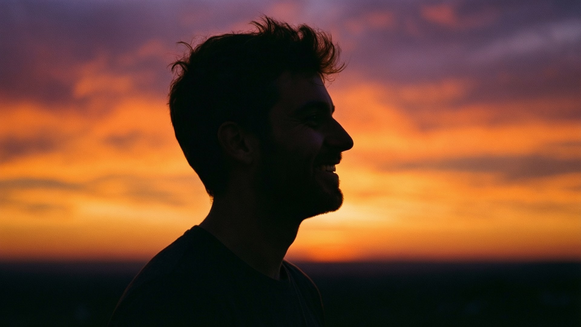 Sunset Smile Silhouette 壁紙 — 一個男人的剪影在充滿活力的橙色和紫色日落天空下微笑。