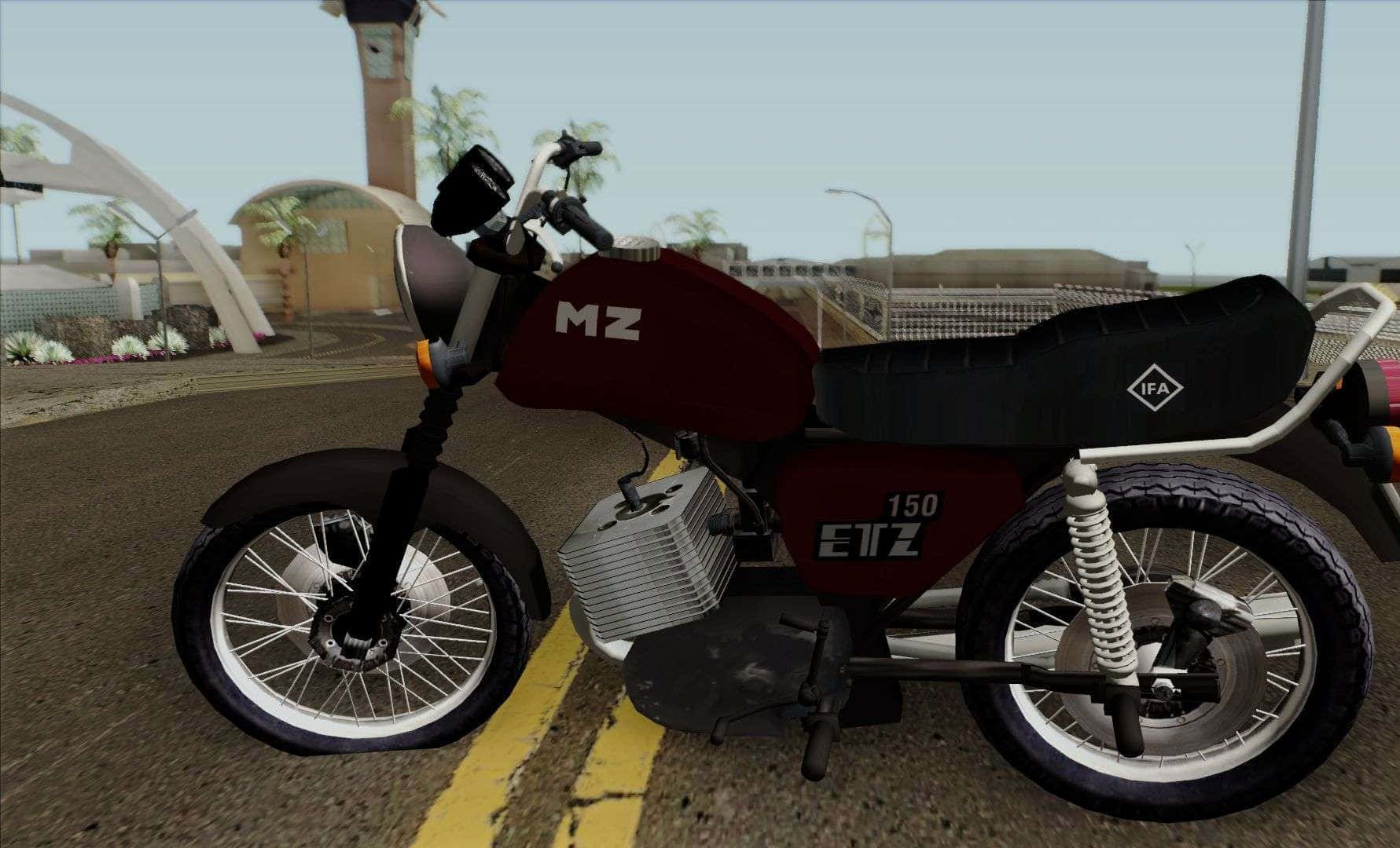 Mz Motorcycle 桌布 壁紙 — 一輛栗色和黑色的150cc機車，配有白色鋼絲輪，停放在現代拱門和棕櫚樹附近的鋪砌道路上。