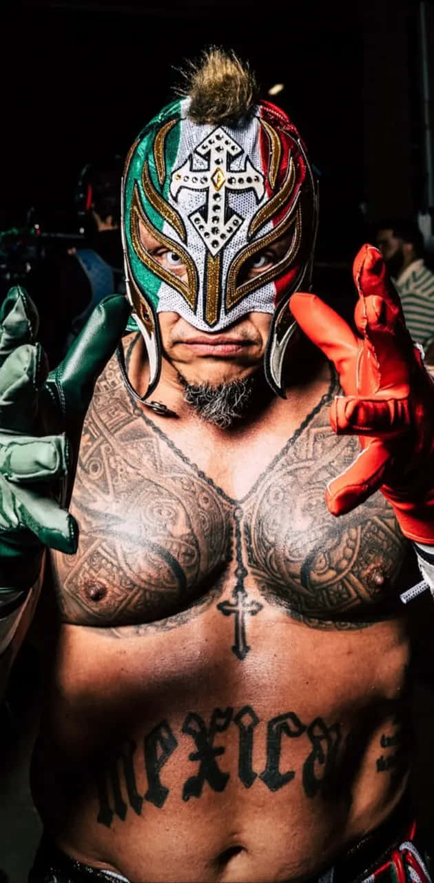  壁紙 — 一位戴著面具的摔角手，身上有複雜的紋身，胸口紋有「Mexico」，在黑暗背景下強烈地擺姿勢。