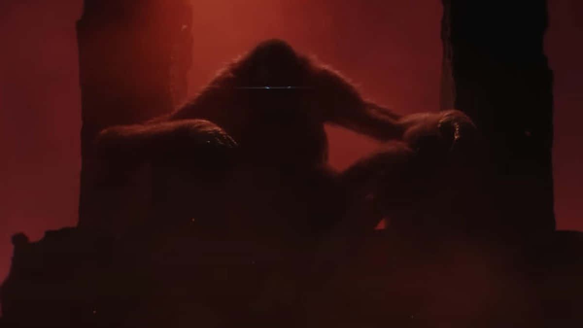 Godzilla X Kong The New Empire 桌布 壁紙 — 一隻巨大的猿坐在廢墟中，以發光的紅色薄霧為背景形成剪影，散發出不祥的力量。