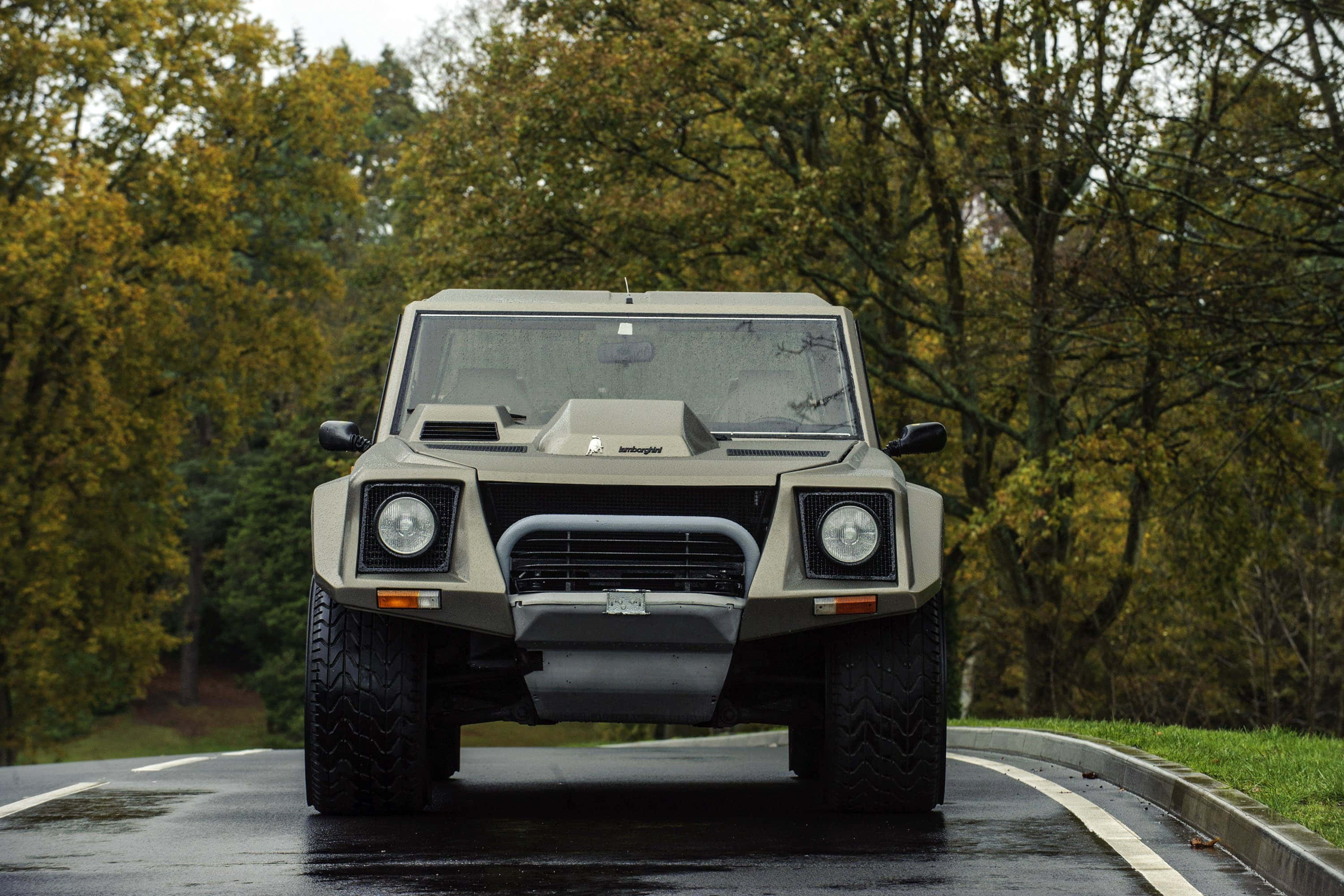 Lamborghini Lm002 桌布 壁紙 — 一輛消光米色的藍寶堅尼LM002大膽地停在潮濕的森林道路上，周圍是秋天的樹木。