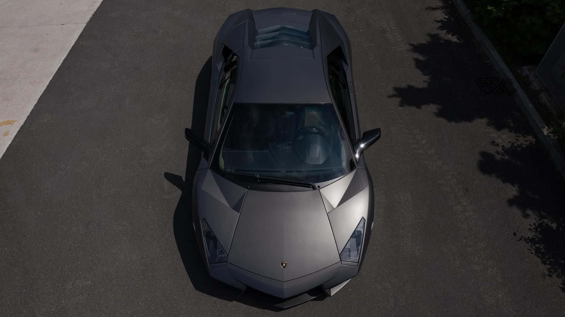 Lamborghini Reventón 桌布 壁紙 — 一輛消光灰色的藍寶堅尼 Aventador 在白天停放在柏油路上，帶有樹影。