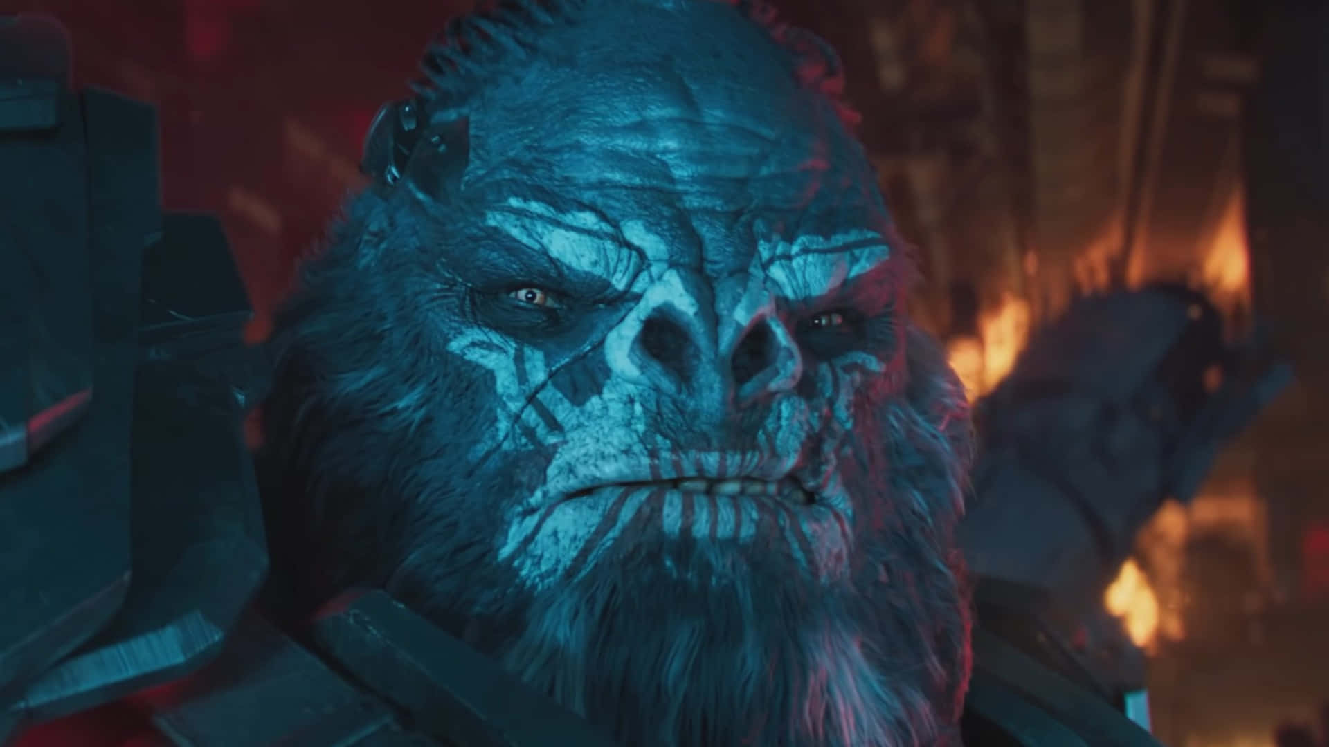 Atriox 桌布 壁紙 — 一隻帶有發光眼睛的威脅性藍皮膚猿猴，在充滿火焰和戰爭的環境中強烈凝視。