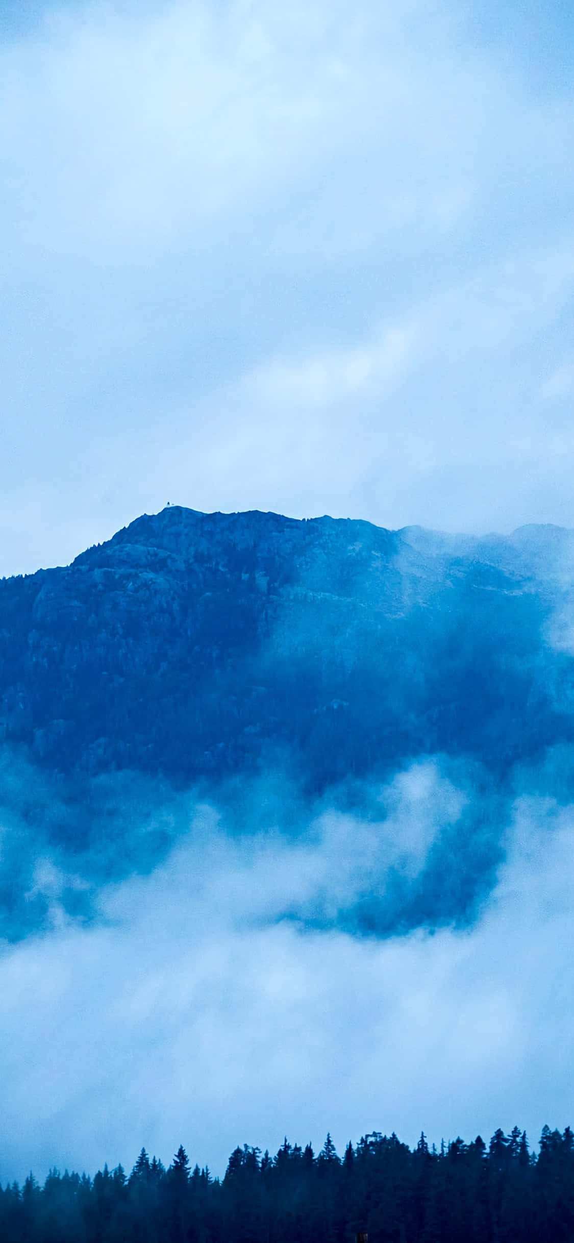 煙霧繚繞的山峰聳立於雲層之上，下方有森林，藍天 — iPhone X 壁紙