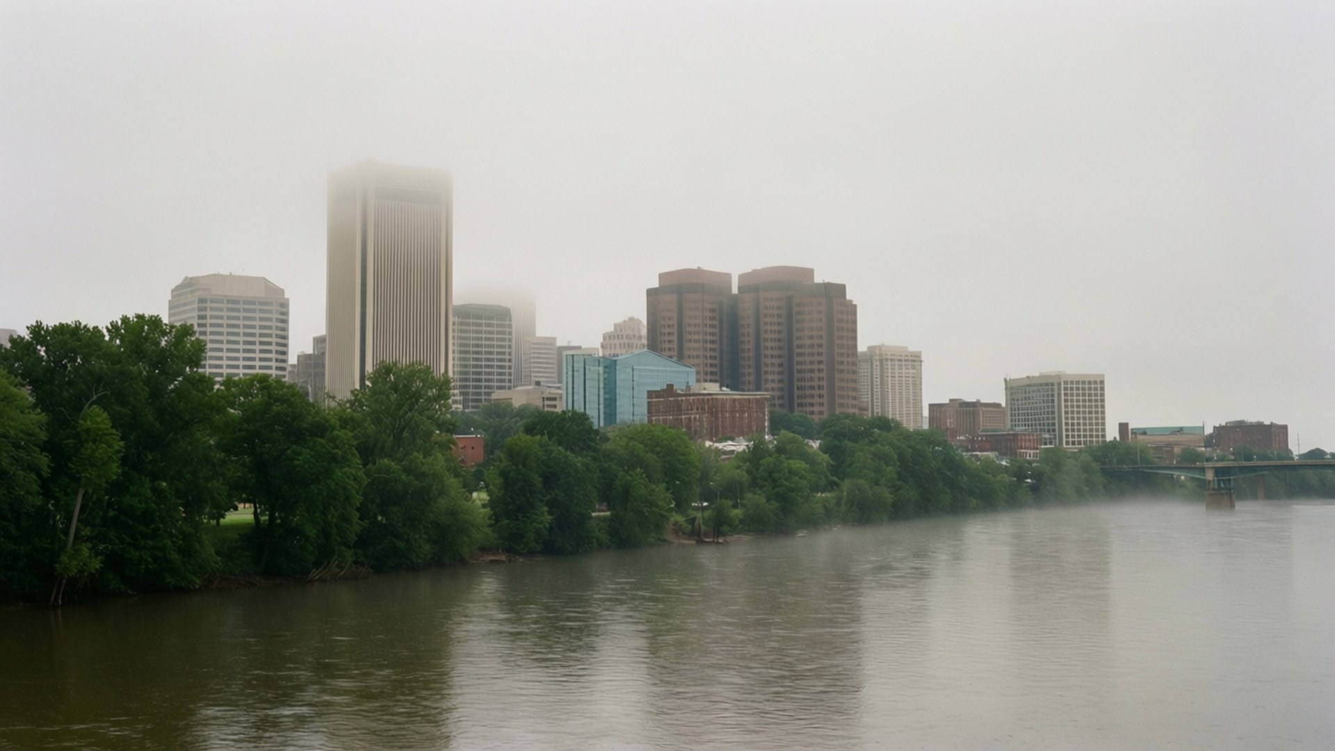 James River Fog 壁紙 — 一條霧氣瀰漫的河流映照出城市天際線，高樓大廈部分被霧遮擋，茂密的綠樹排列在河岸。