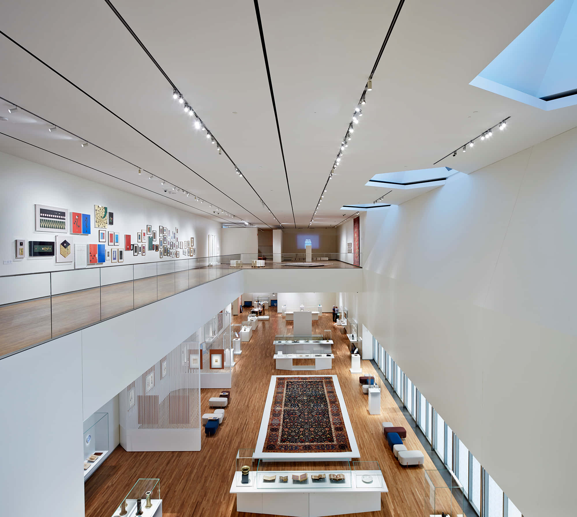 Aga Khan Museum 桌布 壁紙 — 現代藝術博物館，高天花板、木地板，中央有華麗地毯，在明亮的軌道燈光下。