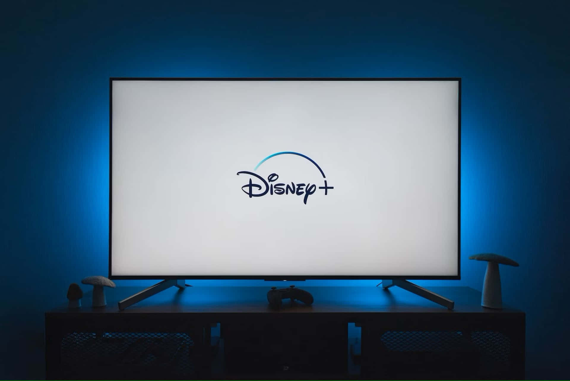  壁紙 — 一台現代電視在極簡娛樂設置中，顯示Disney+標誌，背景是發光的藍色環境光。