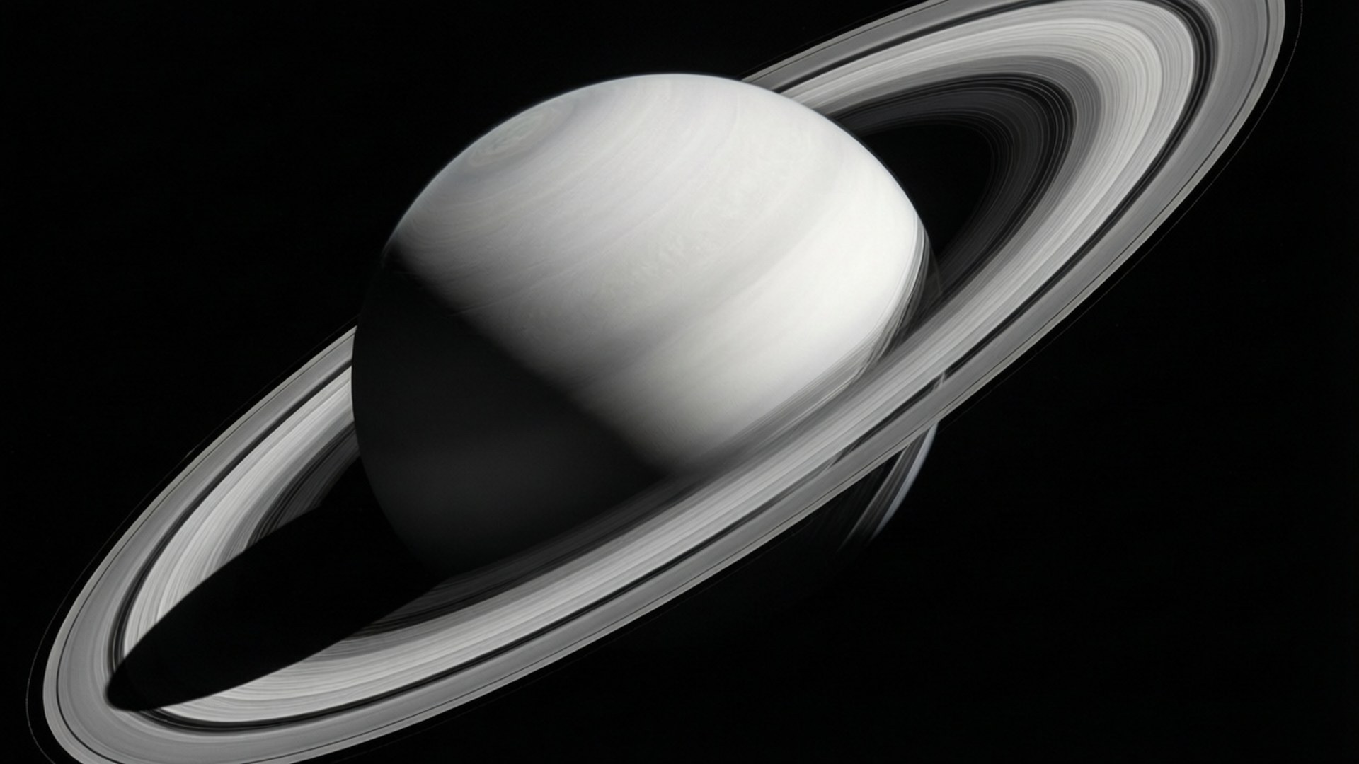 Monochrome Saturn 壁紙 — 土星的單色視圖，其複雜的環系統在太空的虛空中投下銳利的陰影。