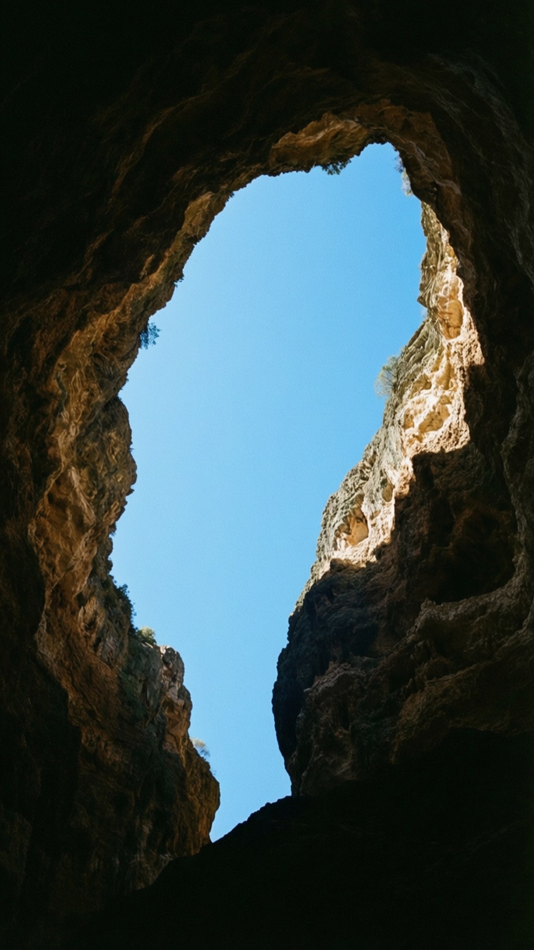 Cave Framed Sky View 壁紙 — 天然岩石拱門框住黑暗洞穴開口上方的清澈藍天。