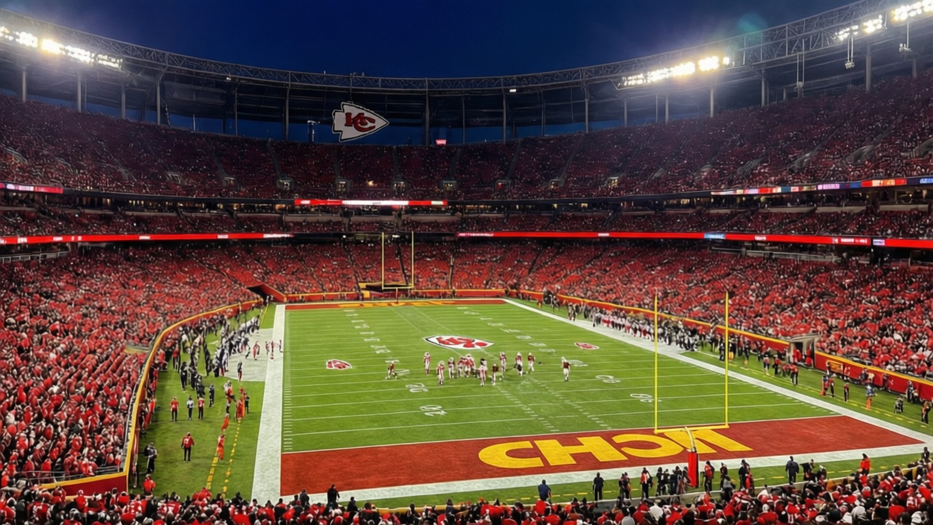 End Zone View 壁紙 — 夜晚擠滿人的體育場，身穿紅衣的球迷在歡呼，球員在明亮的燈光下在綠色場地上列隊。