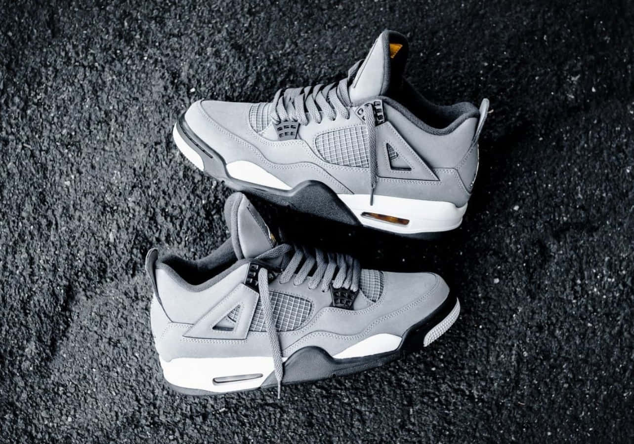 灰色Jordan 4運動鞋搭配白色鞋底，位於深色瀝青表面。 — Air Jordan 壁紙