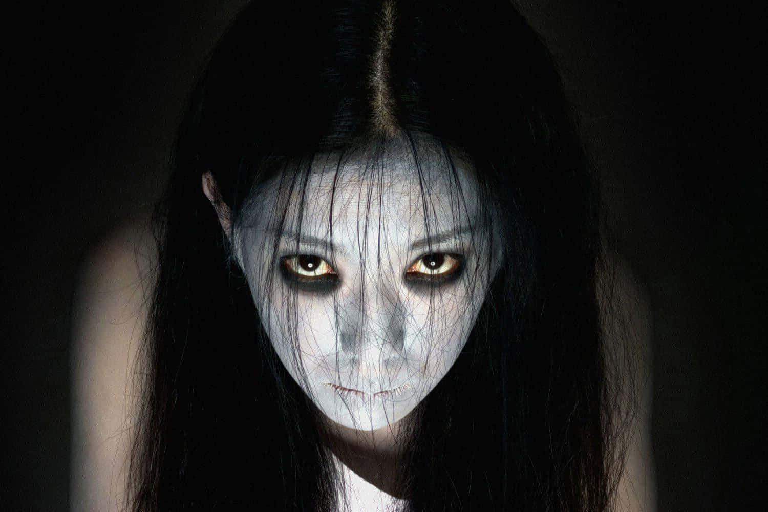  壁紙 — 一個蒼白鬼魅的女人，琥珀色發光的眼睛從黑暗中凝視，構成令人毛骨悚然的恐怖肖像。