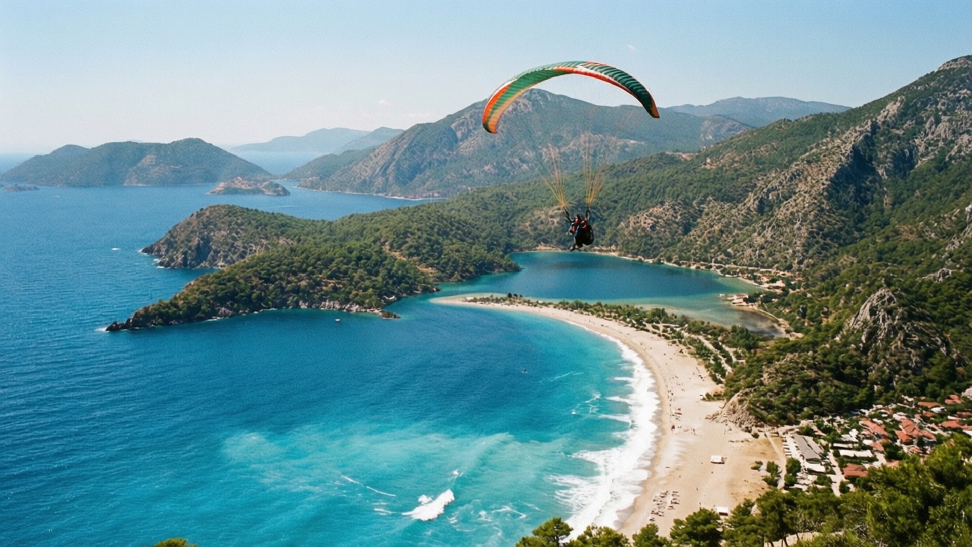 Ölüdeniz Blue Lagoon 壁紙 — 滑翔傘在碧綠海灣上空翱翔，海灣有沙灘坐落在森林覆蓋的山脈之間。