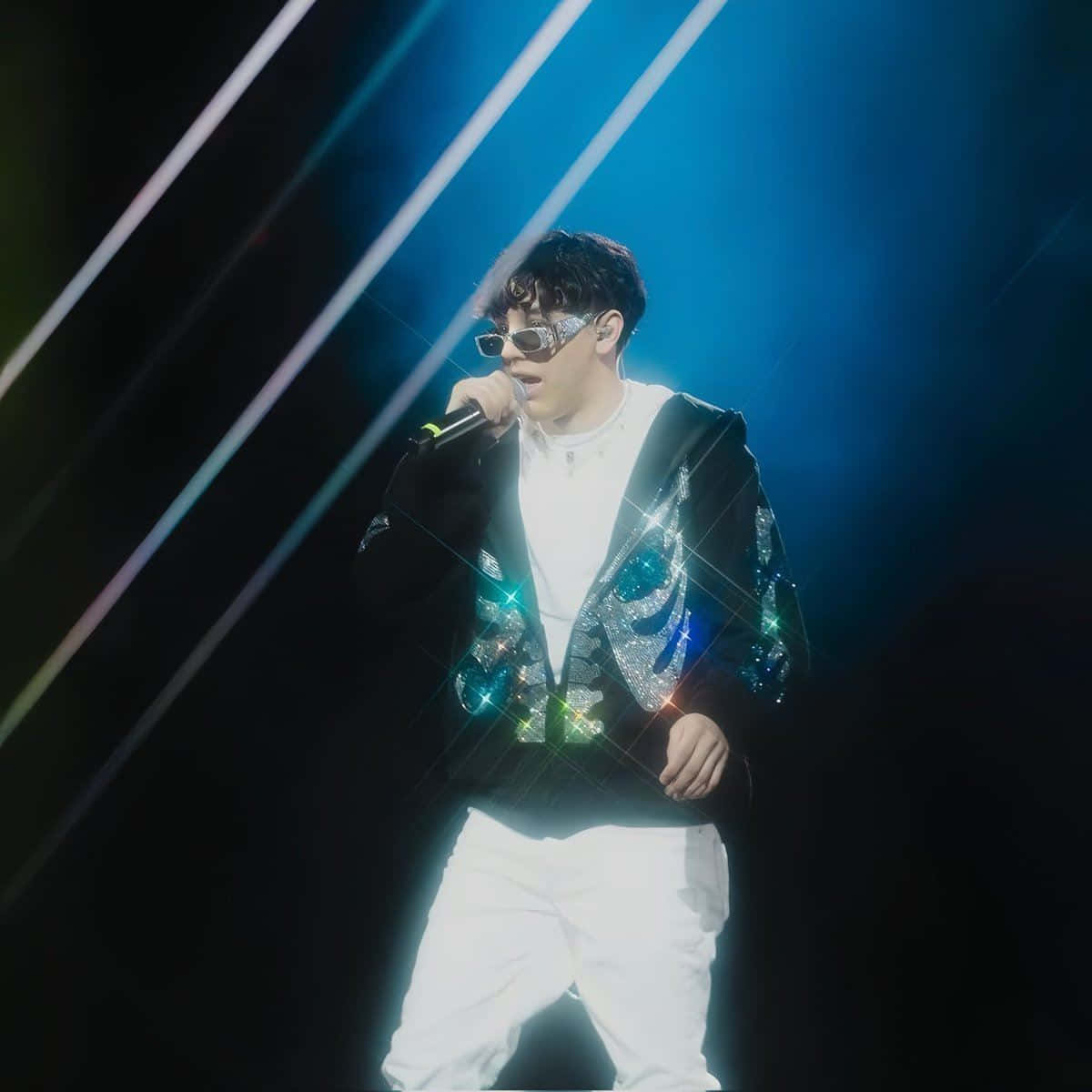  壁紙 — 一位身穿閃亮外套和太陽眼鏡的表演者在戲劇性的藍色舞台燈光下對著麥克風唱歌。
