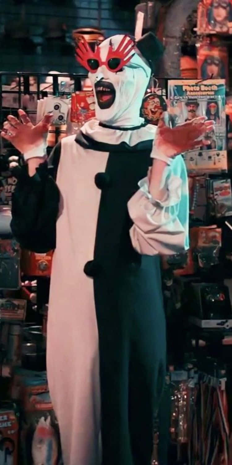  壁紙 — 一個穿著恐怖小丑服裝、眼睛塗成紅色、身穿黑白分體服裝的人站在雜亂的玩具店裡。