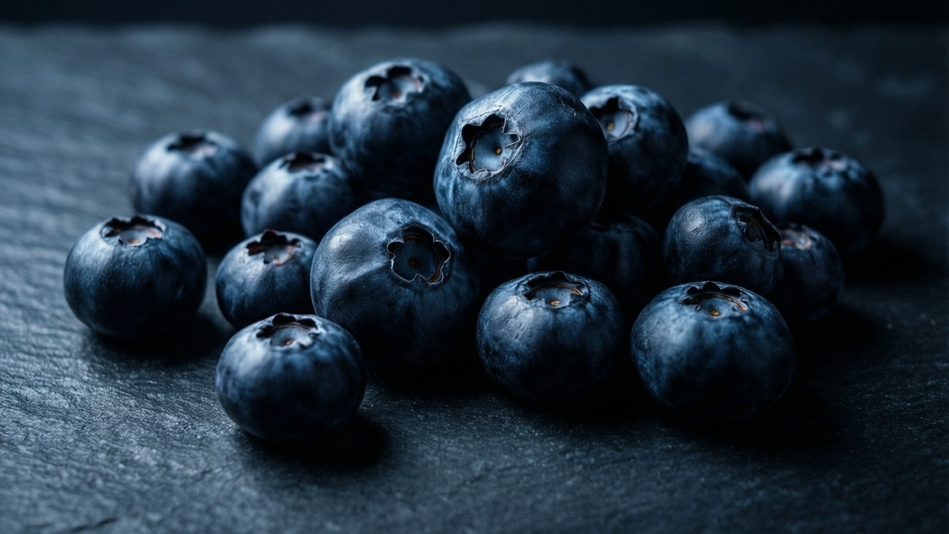 Midnight Blueberries 壁紙 — 一堆飽滿深色藍莓帶有灰塵的果皮，放在有紋理的板岩表面上，燈光營造氣氛。