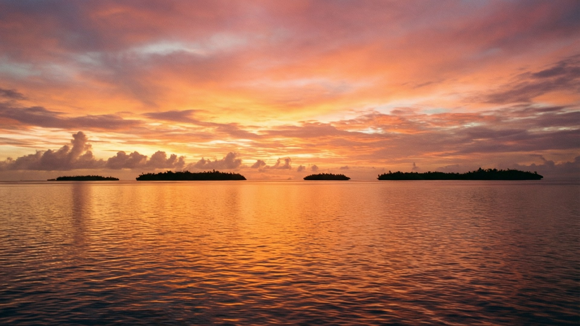 Ha'apai Sunset 壁紙 — 平靜水域上的寧靜日落，剪影島嶼反射出熾熱的橙色和粉紅色雲彩。