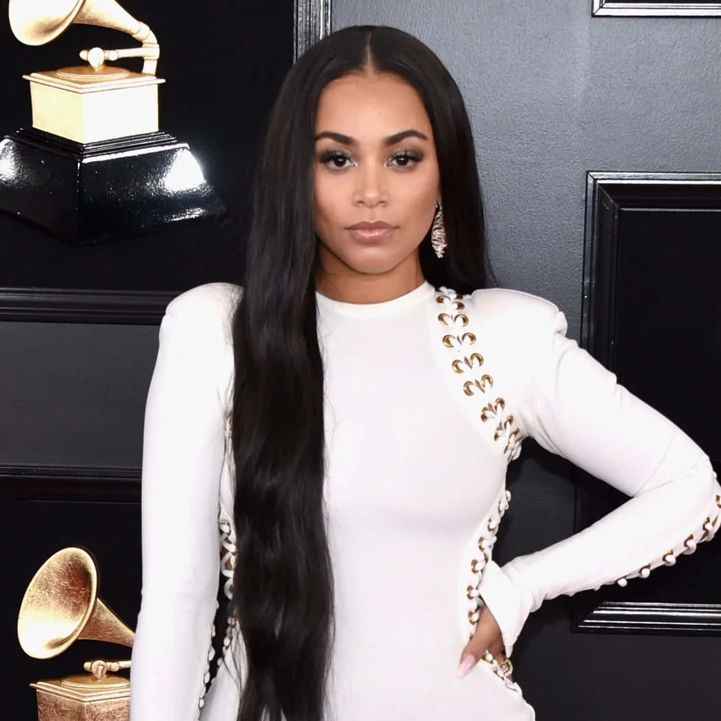 Lauren London 桌布 壁紙 — 一位身穿白色禮服、飾有金色裝飾的優雅女性，自信地站在黑色背景前的葛萊美獎座旁。