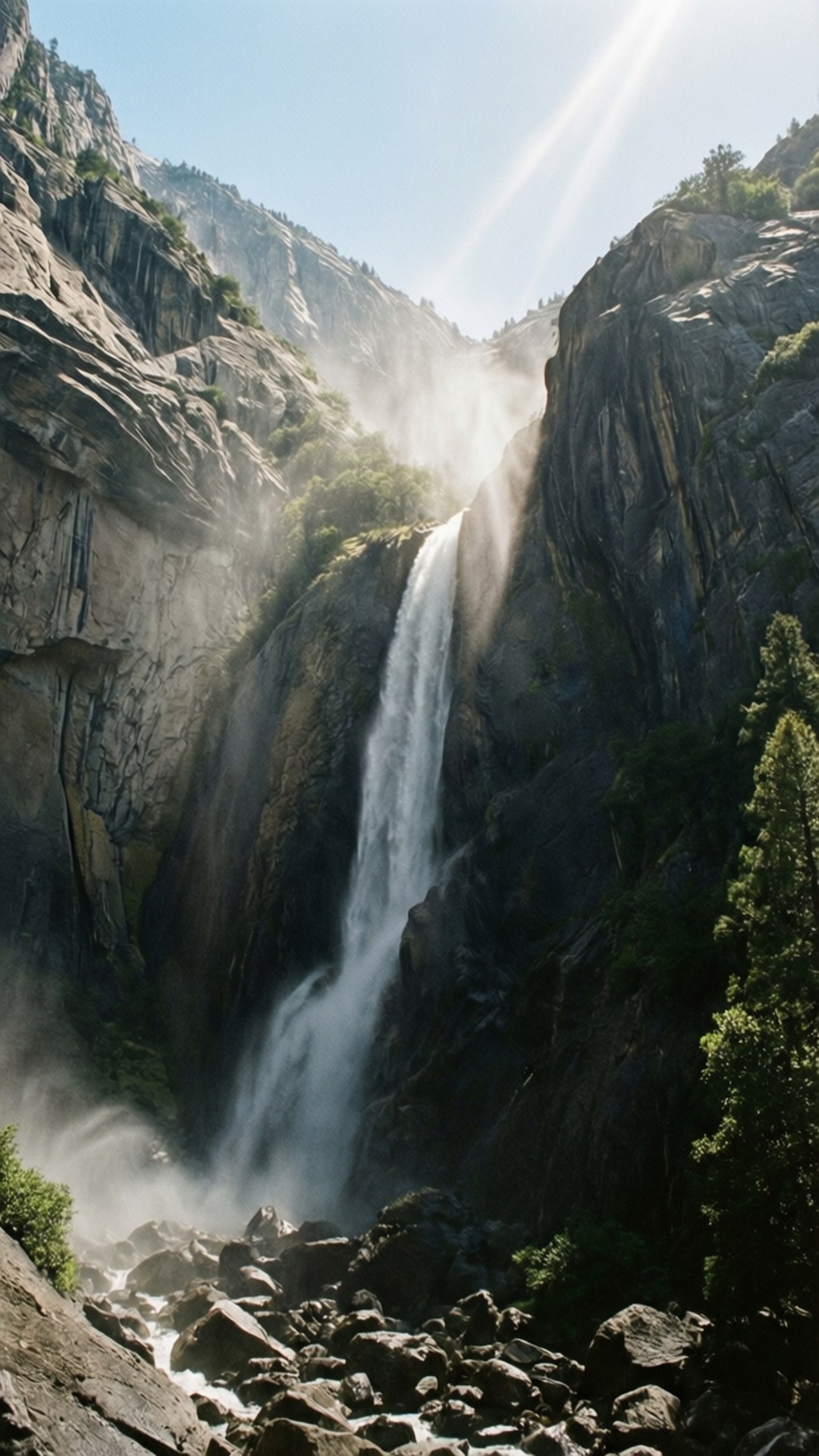 Looking Up at Yosemite Falls 壁紙 — 一道強勁的瀑布從崎嶇的懸崖上傾瀉而下，霧氣升騰，陽光穿過峽谷照射進來。