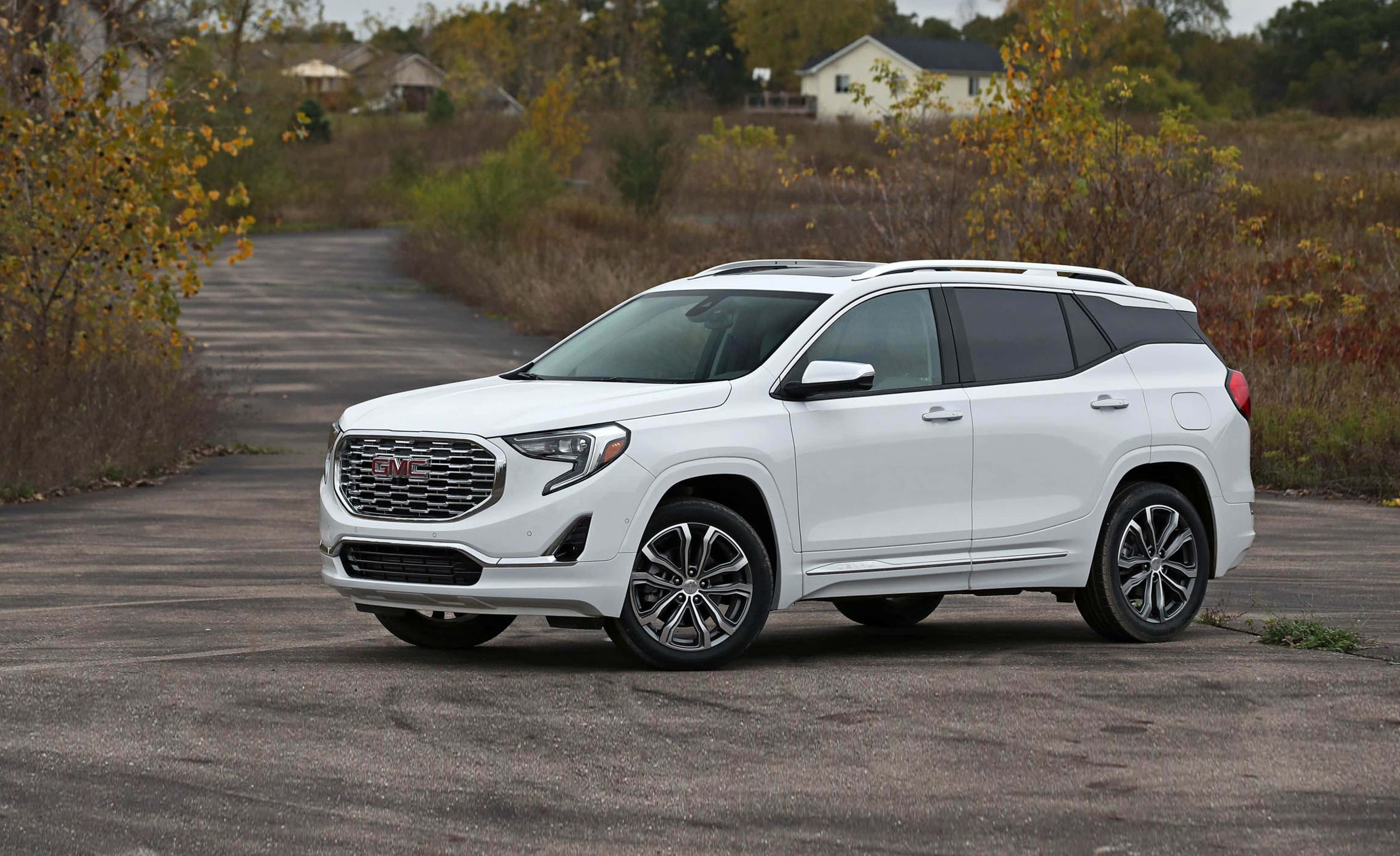 Gmc Terrain 桌布 壁紙 — 一輛純白色的GMC Terrain SUV停放在碎石車道上，周圍環繞著秋葉和遠處的房屋。