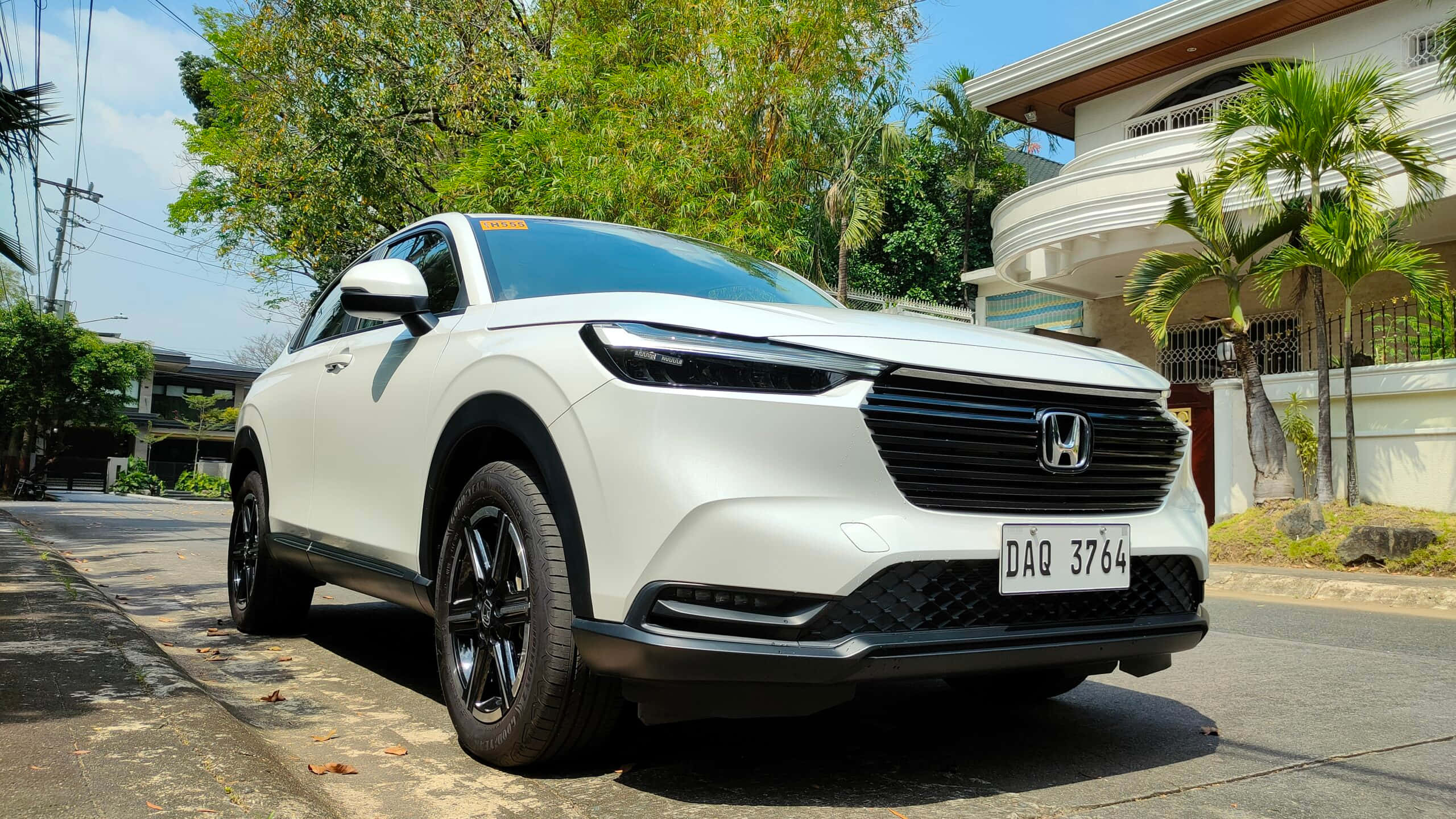 Honda Hr-v 桌布 壁紙 — 一輛純白色的本田SUV停放在陽光普照的住宅街道上，街道兩旁種滿茂密的綠樹，還有一座白色房子。