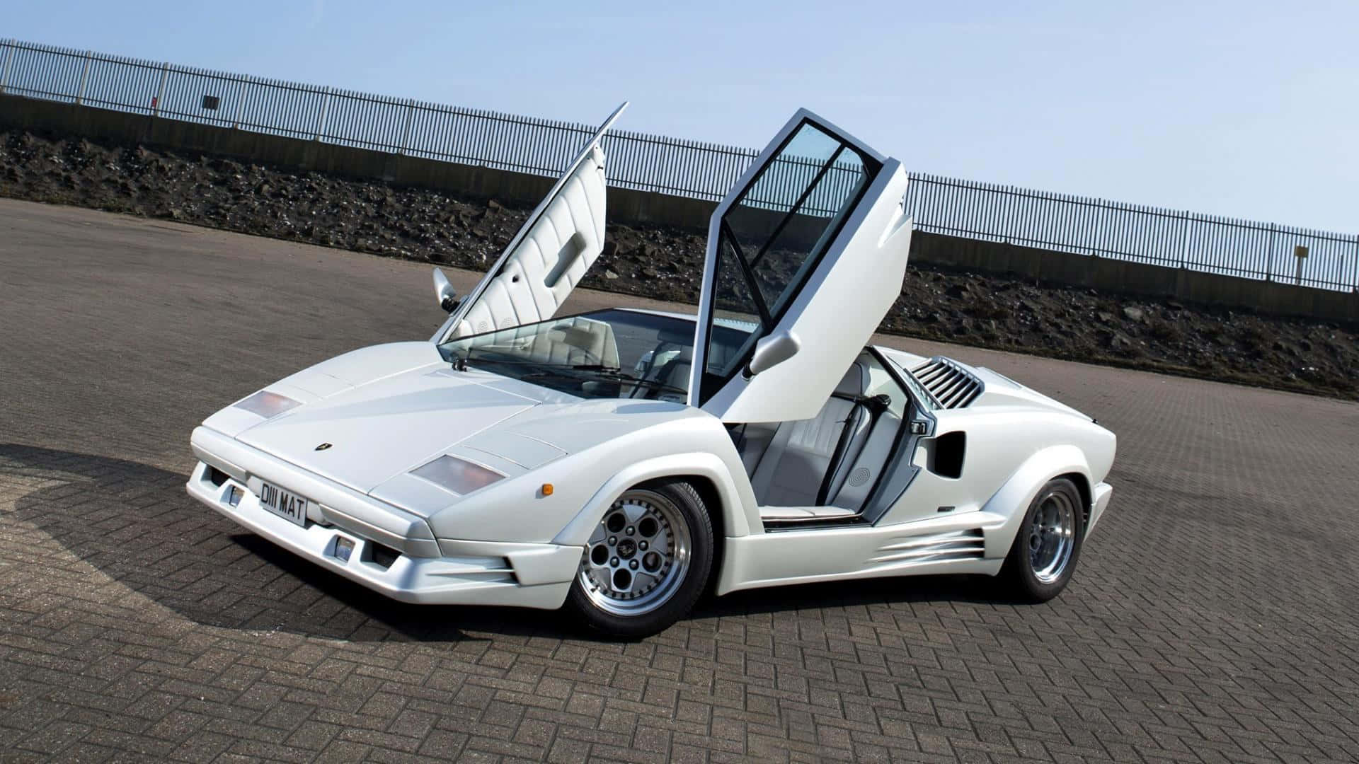 Lamborghini Countach 桌布 壁紙 — 一輛純白色的藍寶堅尼Countach，剪刀門打開，停在鋪砌路面上，天空晴朗。