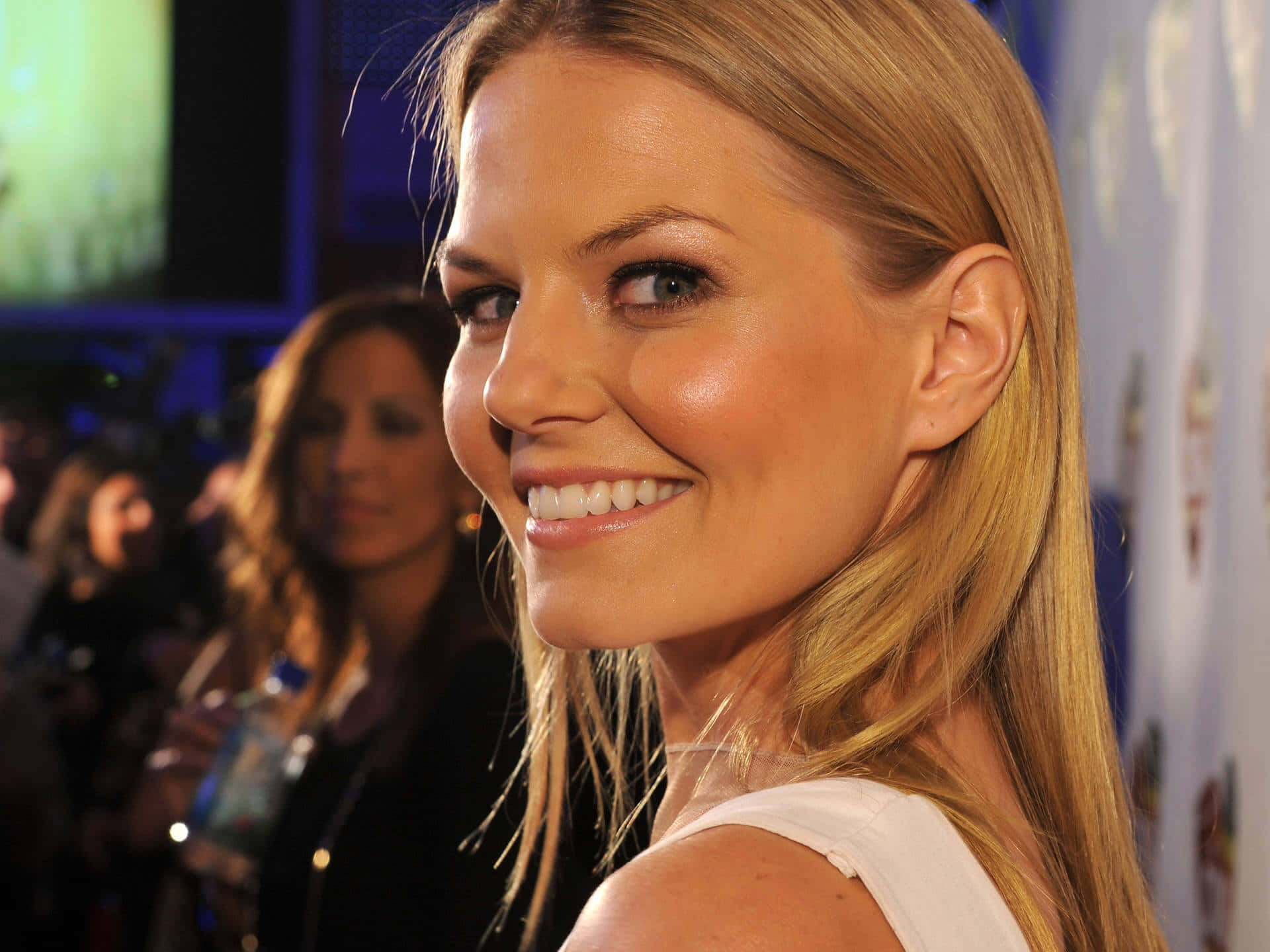jennifer morrison 桌布 壁紙 — 一位光彩照人的金髮女子在一個華麗的活動中對著鏡頭溫暖微笑，身後有模糊的與會者。