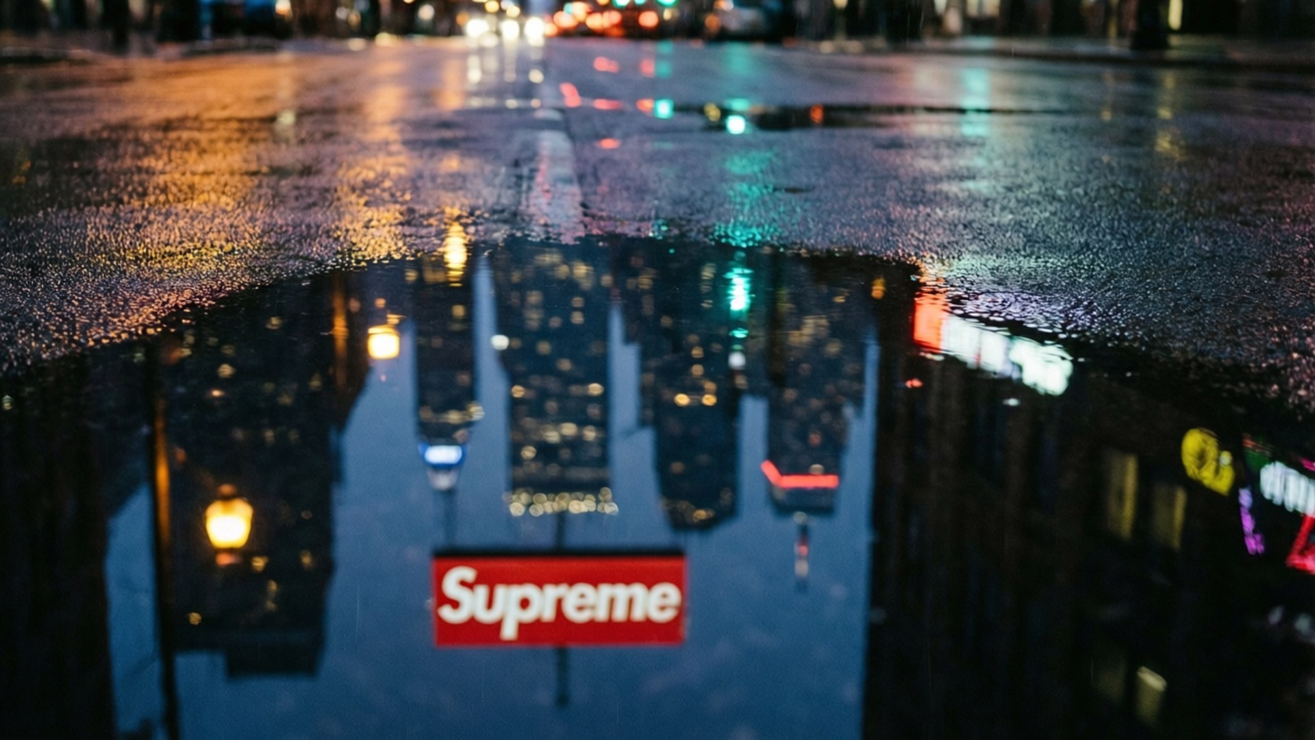 Supreme Skyline Reflection 壁紙 — 城市街道上的雨水坑反射出霓虹燈和夜間發光的紅色Supreme標誌。