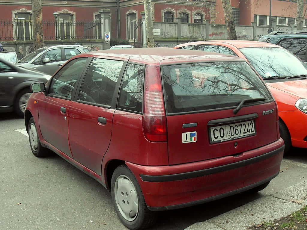 Fiat Punto 桌布 壁紙 — 一輛紅色Fiat Panda停放在城市街道上，背景有光禿禿的樹木和磚造建築。